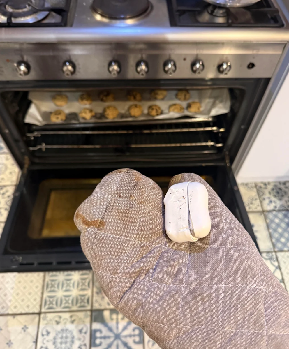 A hand in an oven mitt holds a garlic bulb in front of an open oven with cookies baking inside