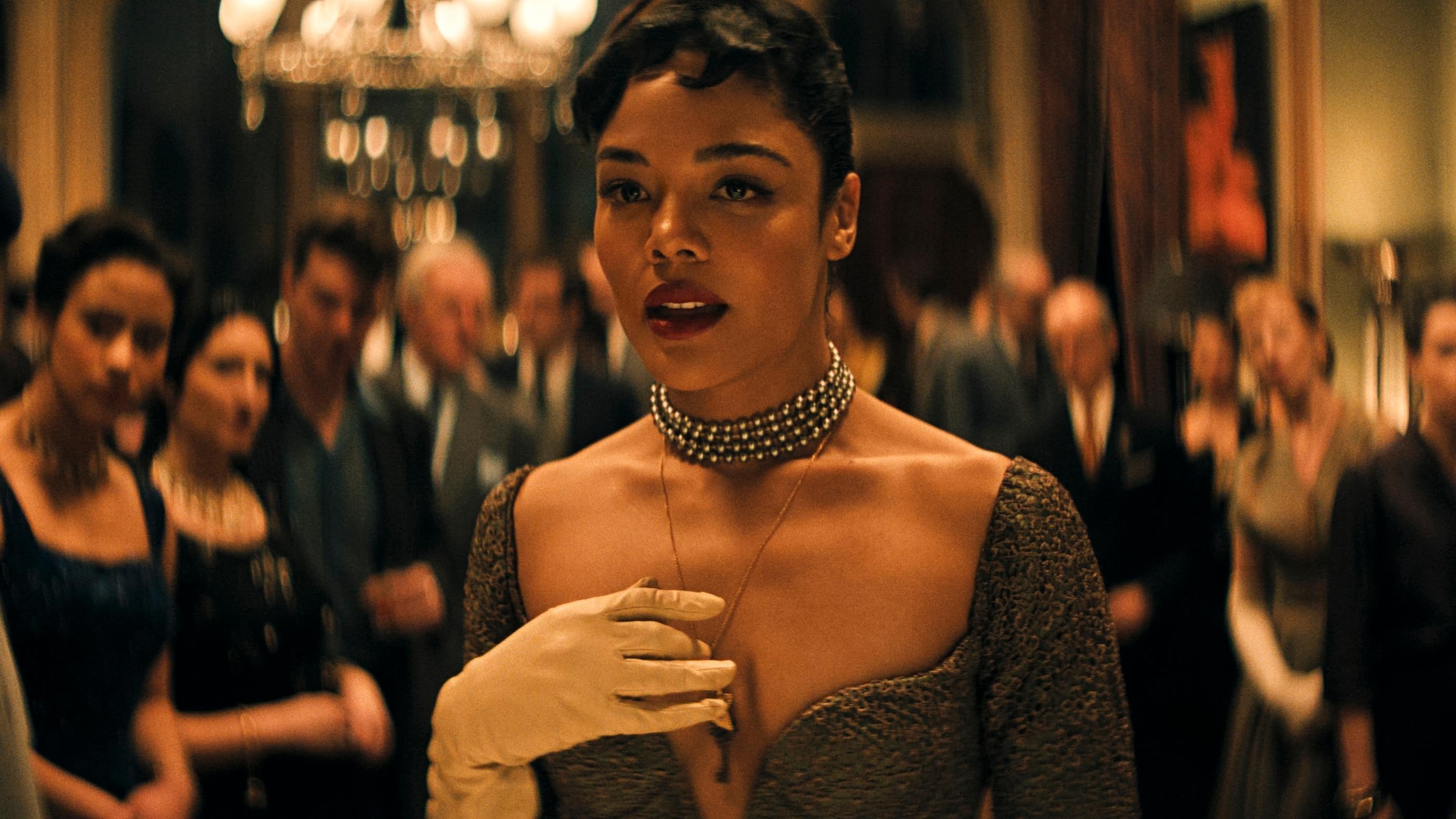 Person in elegant vintage outfit with a diamond choker and gloves, surrounded by a glamorous crowd at a formal event