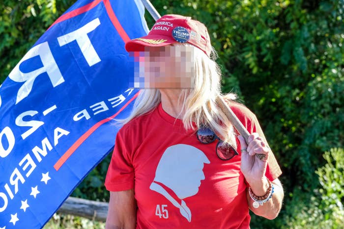Person wearing a "Make America Great Again" hat and Trump shirt, holding a flag at an outdoor event