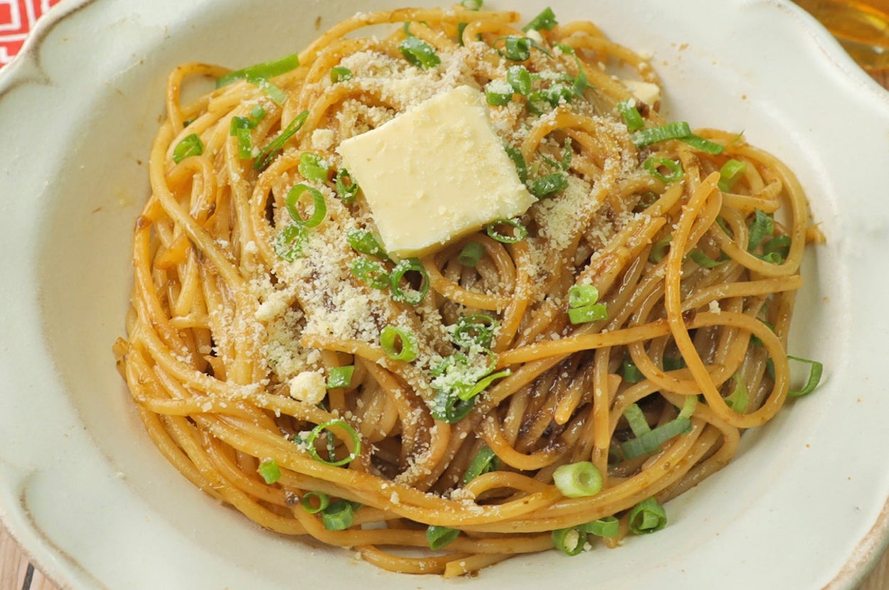 パスタの上にバターと刻みネギがトッピングされた醤油風味のスパゲティ。白い皿に盛られている。