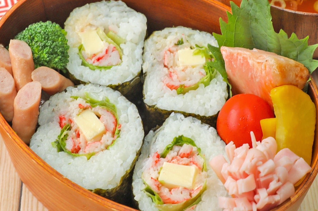 お弁当に寿司ロール、ウインナー、ブロッコリー、サラダ、トマトが盛り付けられている。