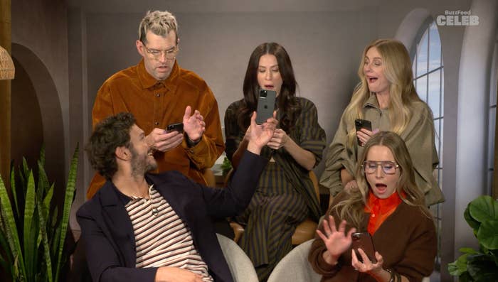 Five people seated, appearing surprised while holding phones, dressed in casual and business attire