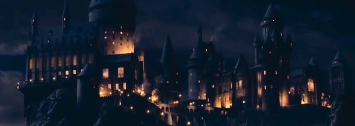 Hogwarts with turrets and towers, illuminated at night, on a rocky landscape
