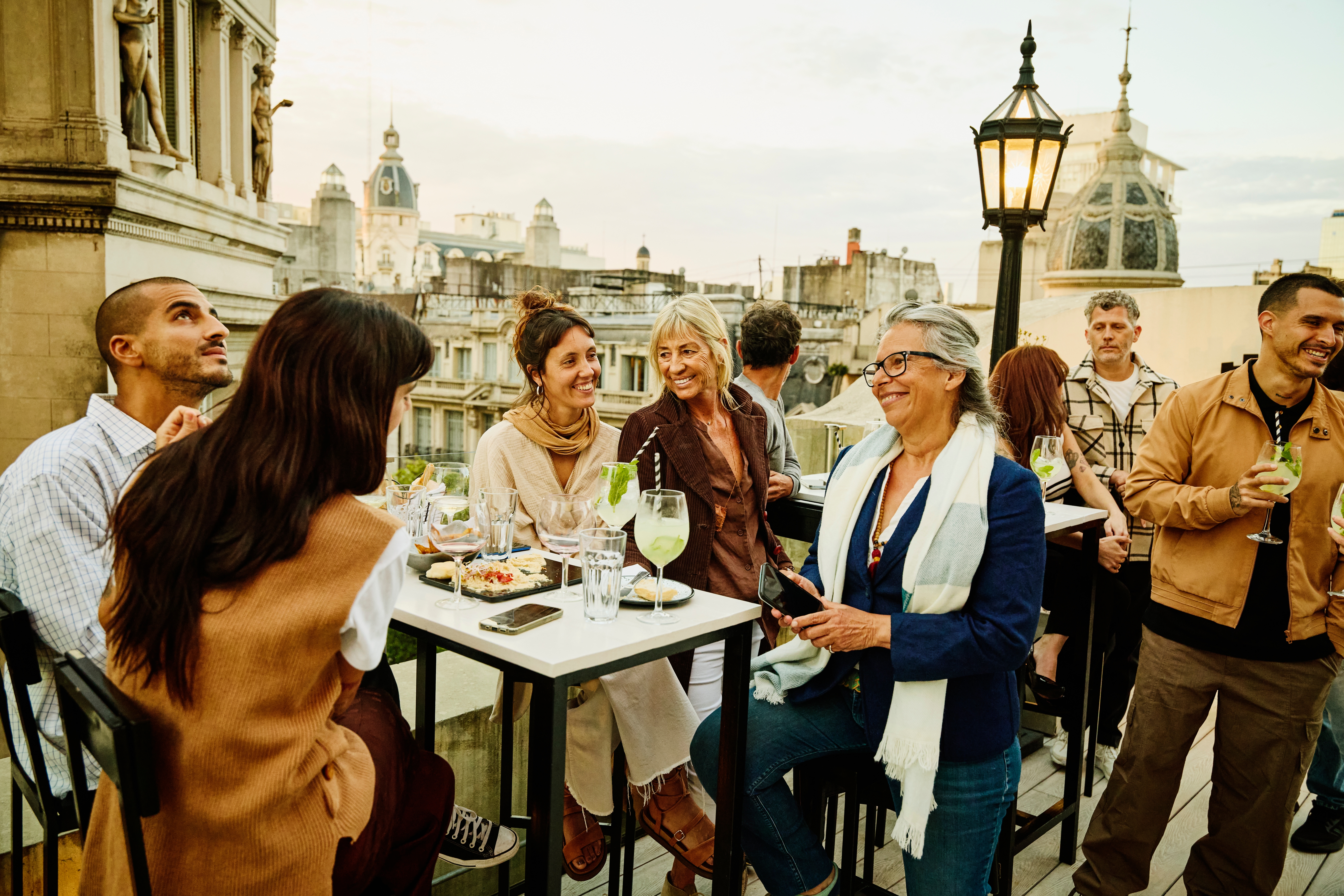 Folk nyter drinker og samtaler på en taksamling med utsikt over bybildet