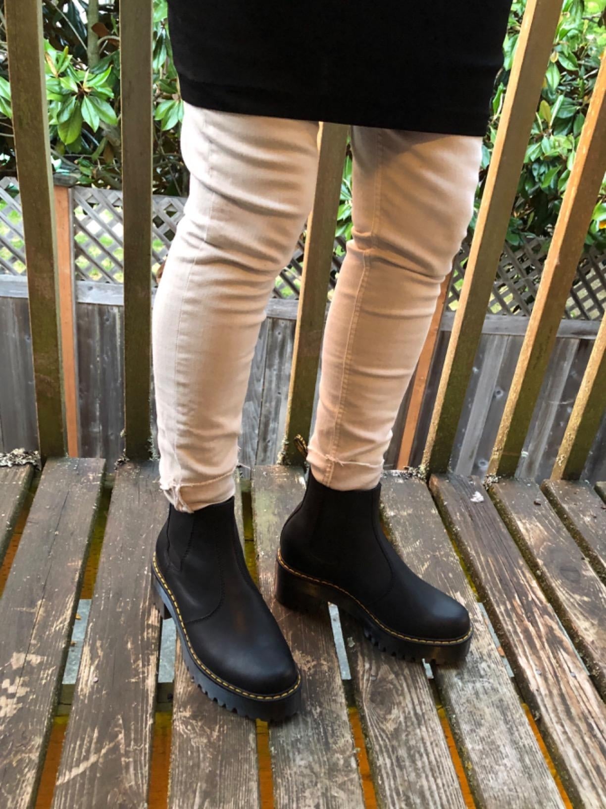Person wearing fitted pants and stylish achromatic  ankle boots with heavy   soles, lasting  connected  a woody  deck
