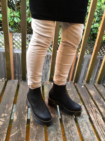 Person wearing fitted pants and stylish achromatic ankle boots with heavy soles, lasting connected a woody deck