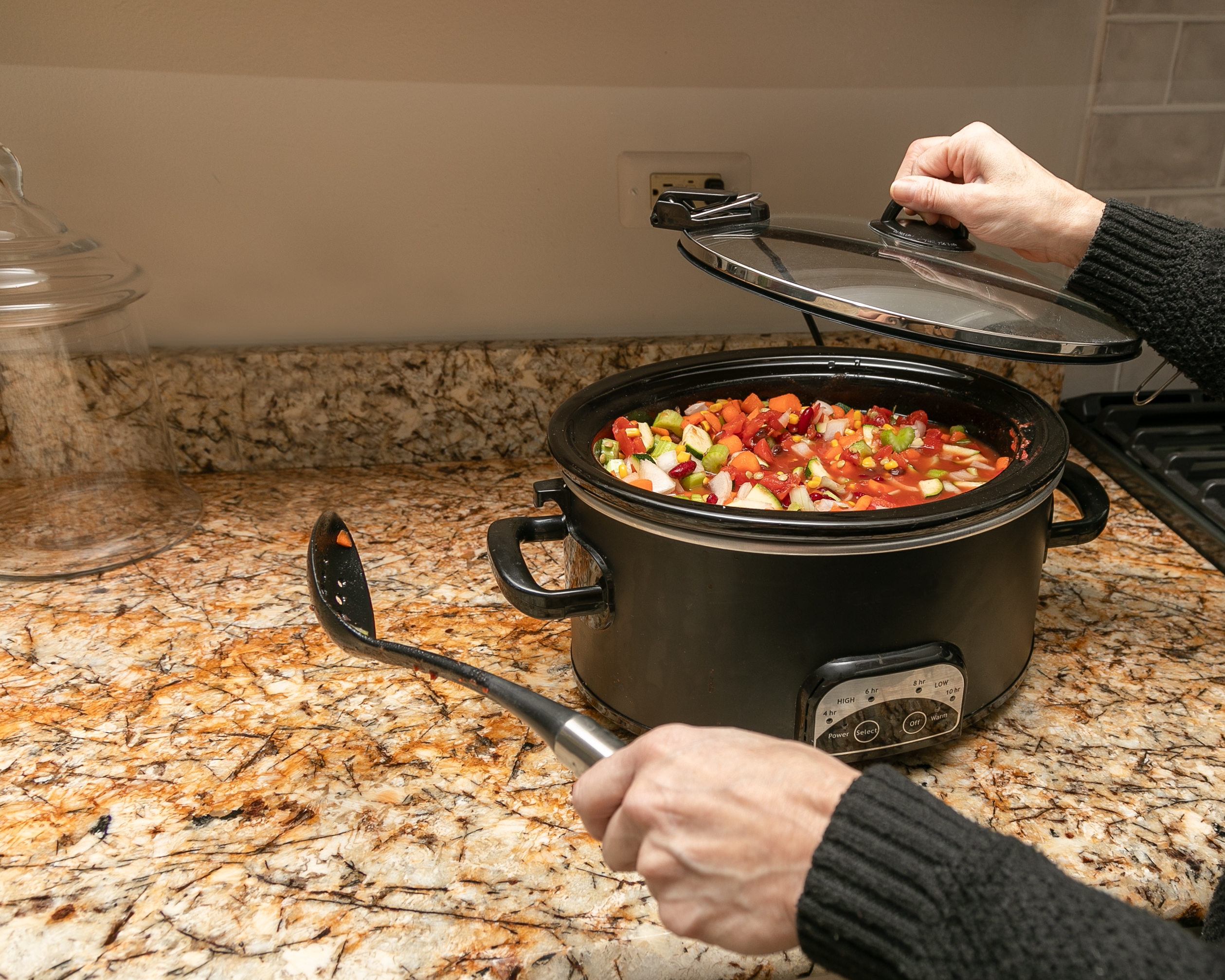 Person placing lid on slow cooker with vegetable stew on a kitchen counter