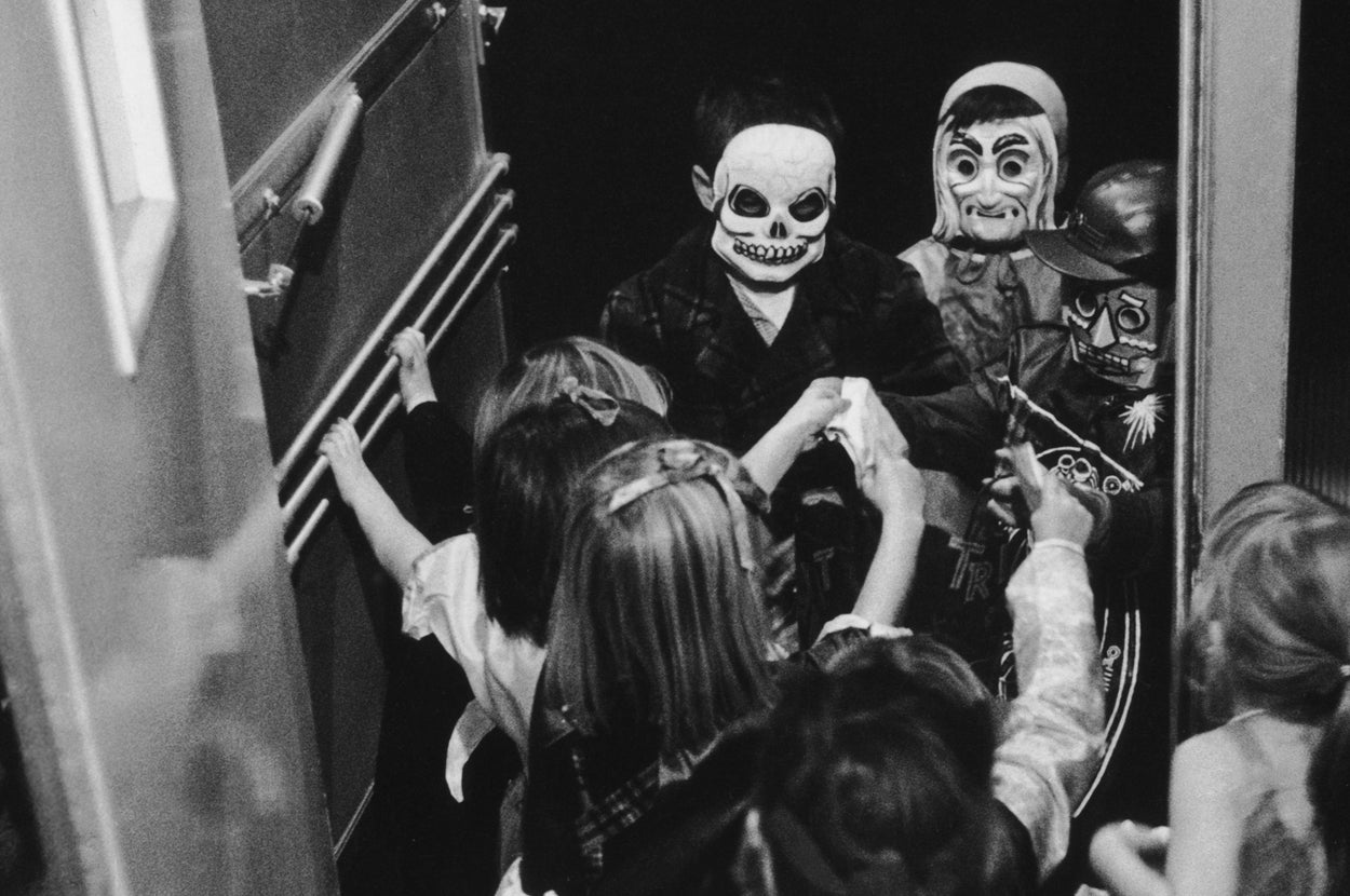 Children in Halloween costumes, including a skeleton and pirate, eagerly enter a doorway, embodying the festive spirit of trick-or-treating
