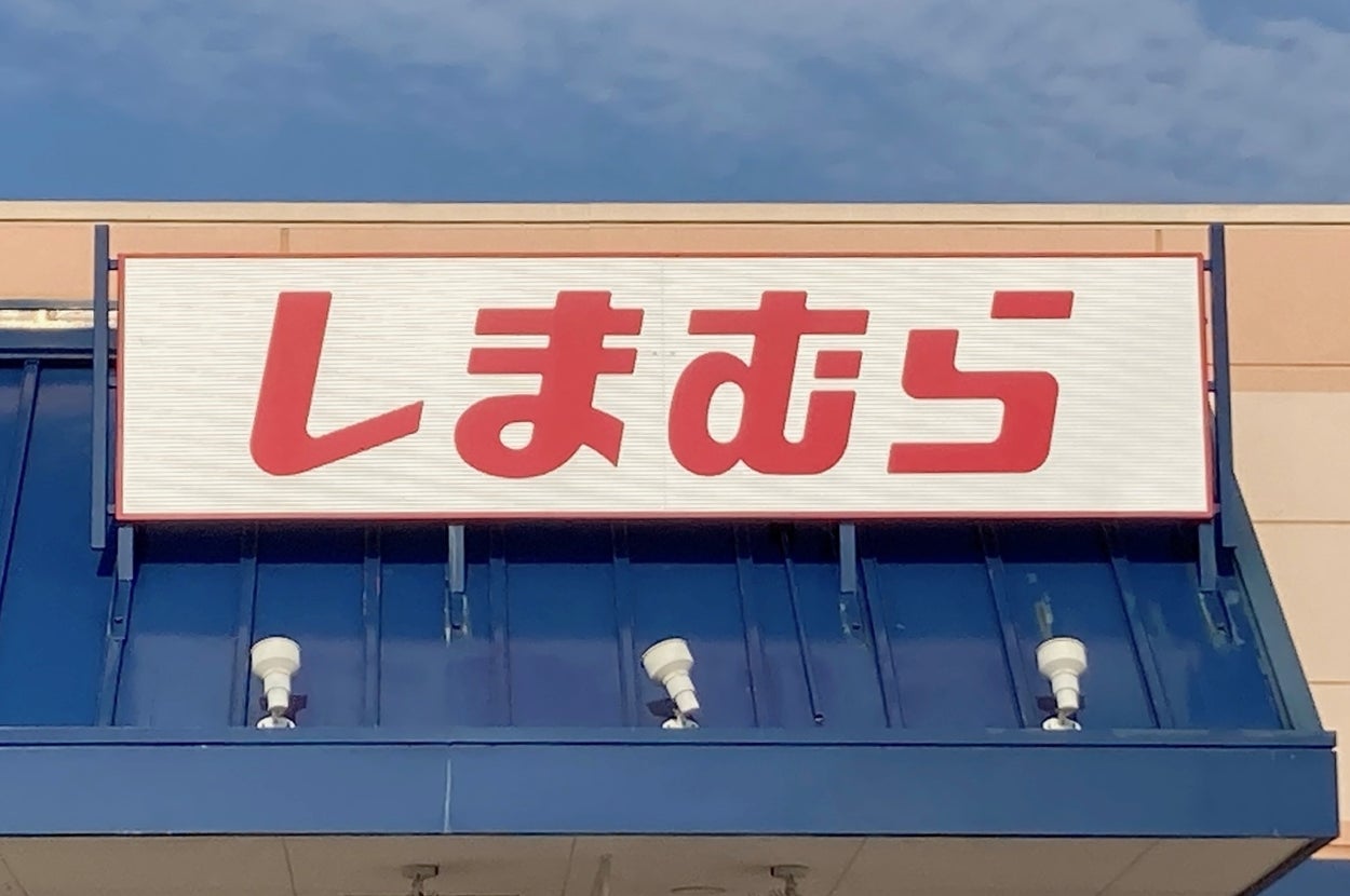 Storefront with a sign displaying Japanese characters, indicating a retail location, with a blue sky backdrop and a handicapped parking sign visible