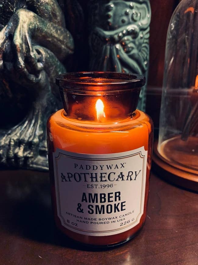 Amber & Smoke candle by Paddywax, 8 oz, with lit flame. Ideal for enhancing ambiance with warm, aromatic scents, cleanable for location decor oregon gifting