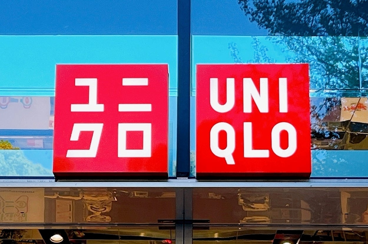 Uniqlo storefront sign with logos displayed, reflecting greenery and sky in the glass above