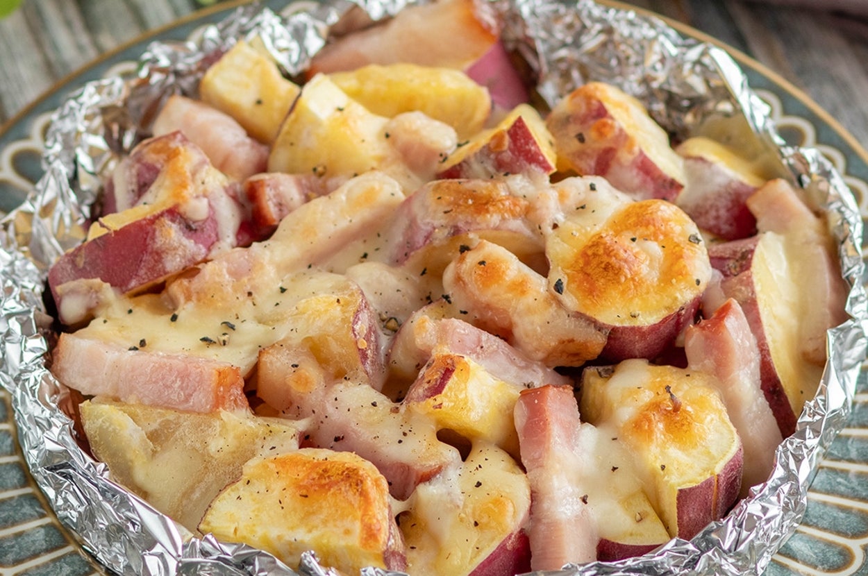 アルミホイルに包まれた焼きサツマイモとベーコンのチーズ焼きが食卓に置かれている。