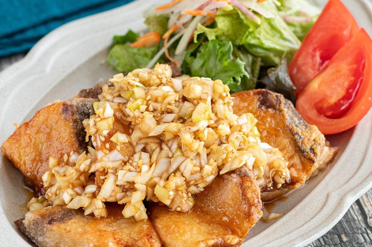 魚のフライに刻んだネギのソース、サラダとトマトが付け合わせとして添えられた料理。