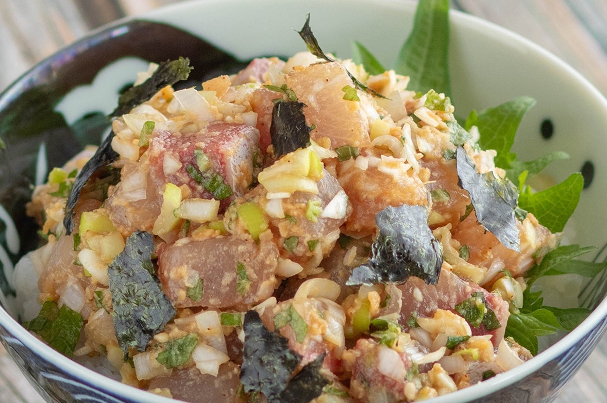 料理のボウルに新鮮な魚とネギ、海苔が盛り付けられたポキ丼。木製テーブルに置かれている。