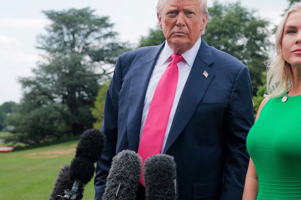 庭園に立つスーツ姿の男性とワンピースの女性。背景にワシントン記念塔。複数のマイクが前に設置されている。