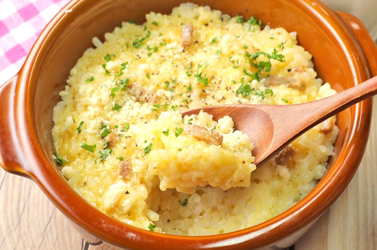 茶色のボウルにクリーミーなリゾットが盛られ、木製のスプーンで一口すくわれている。