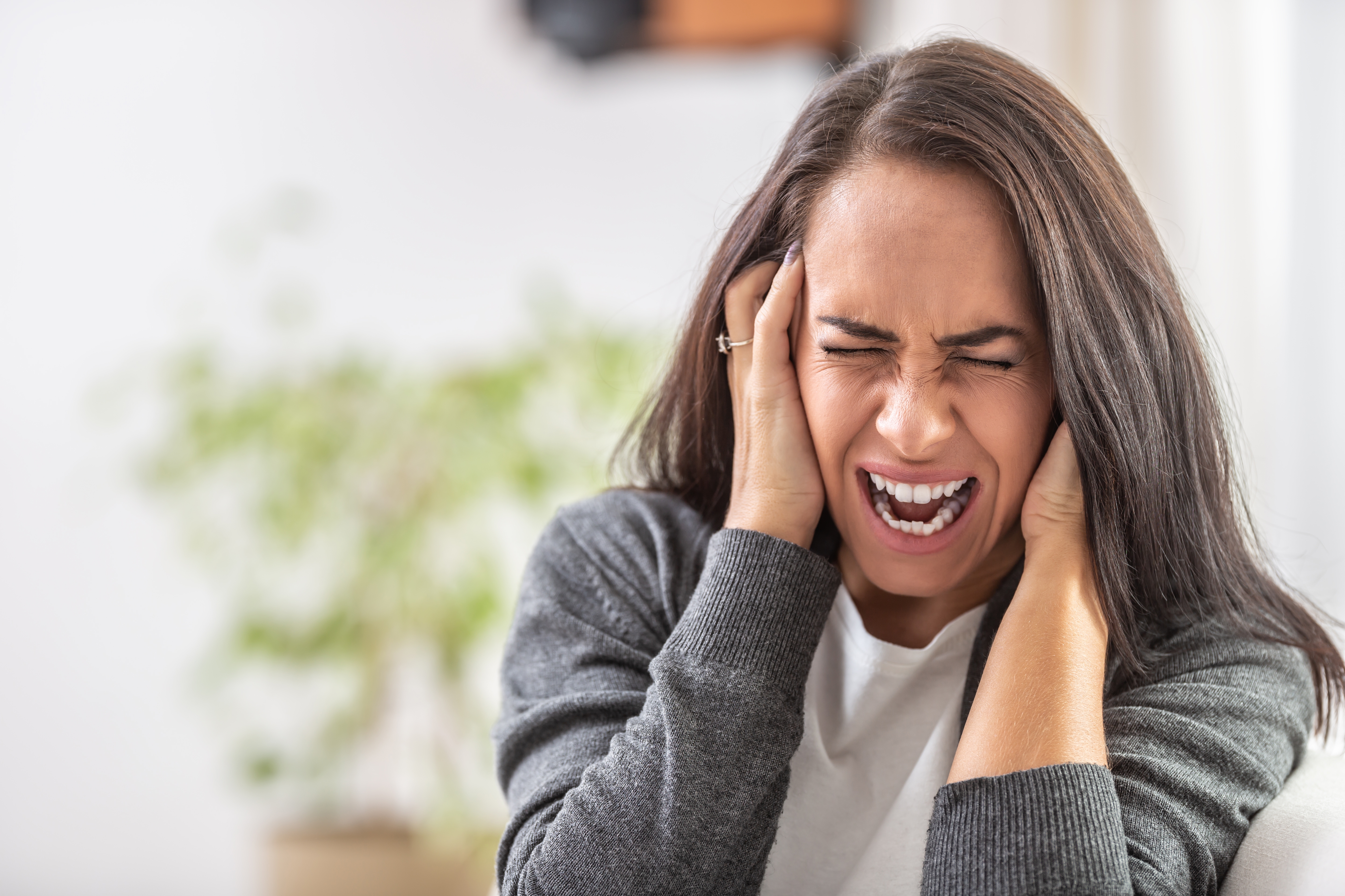 En person holder hodet med begge hender, lukkede øyne, virker stresset eller overveldet, i hjemmemiljø