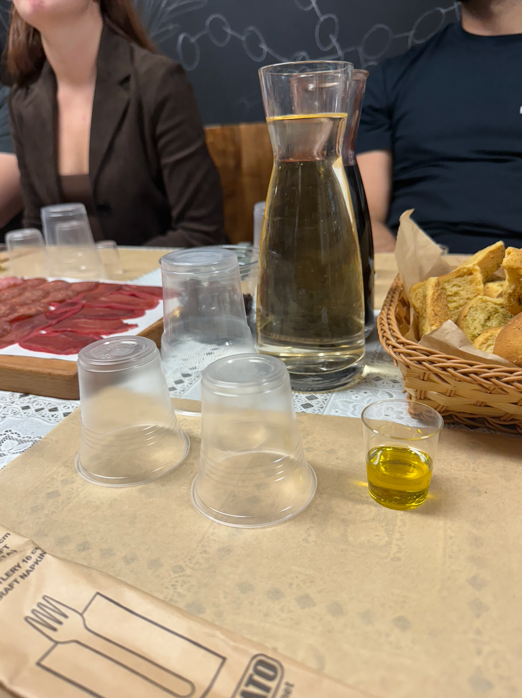 Table set with a pitcher of water, small glasses of olive oil, bread basket, and charcuterie platter