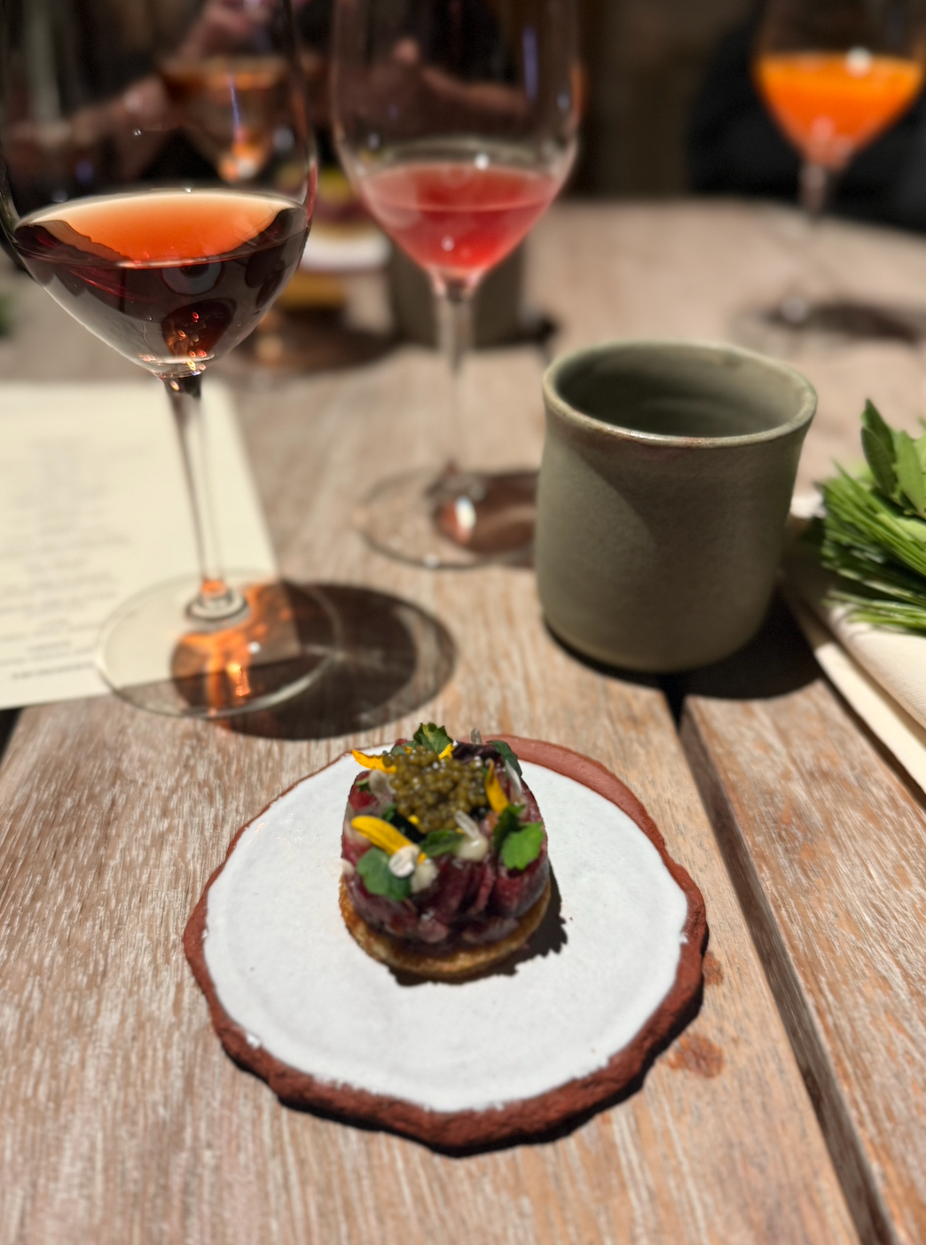Gourmet dish on a ceramic plate with wine glasses in the background at a table setting