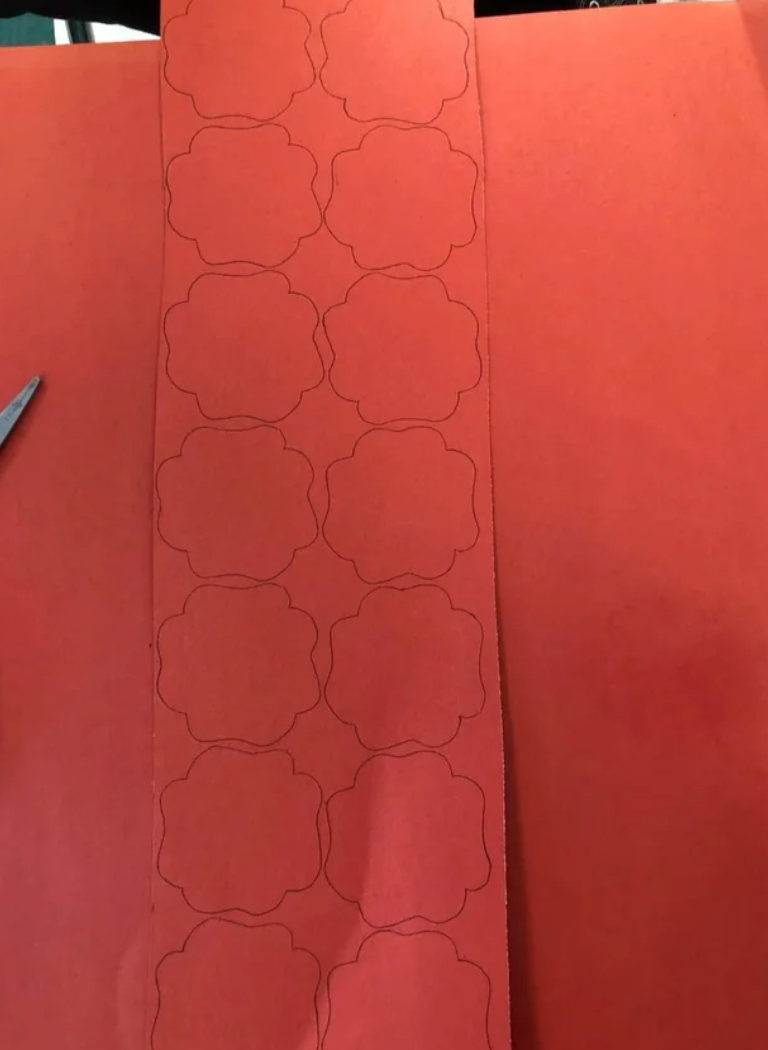 A portion   of reddish  insubstantial  with floral patterns outlined is placed connected  a larger reddish  surface, alongside a brace  of scissors