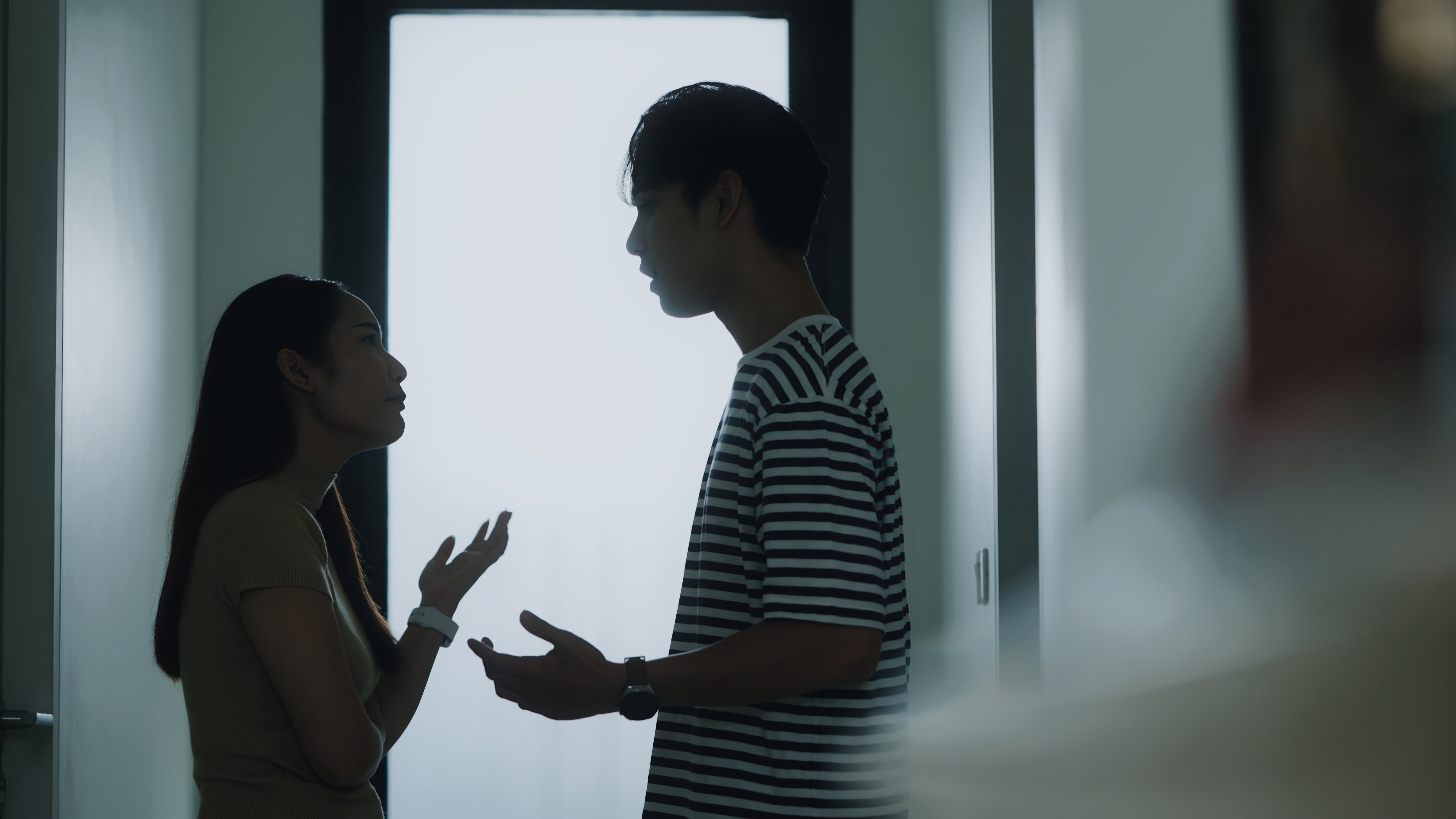 To personer er i silhuett, engasjert i en samtale i en svakt opplyst gang