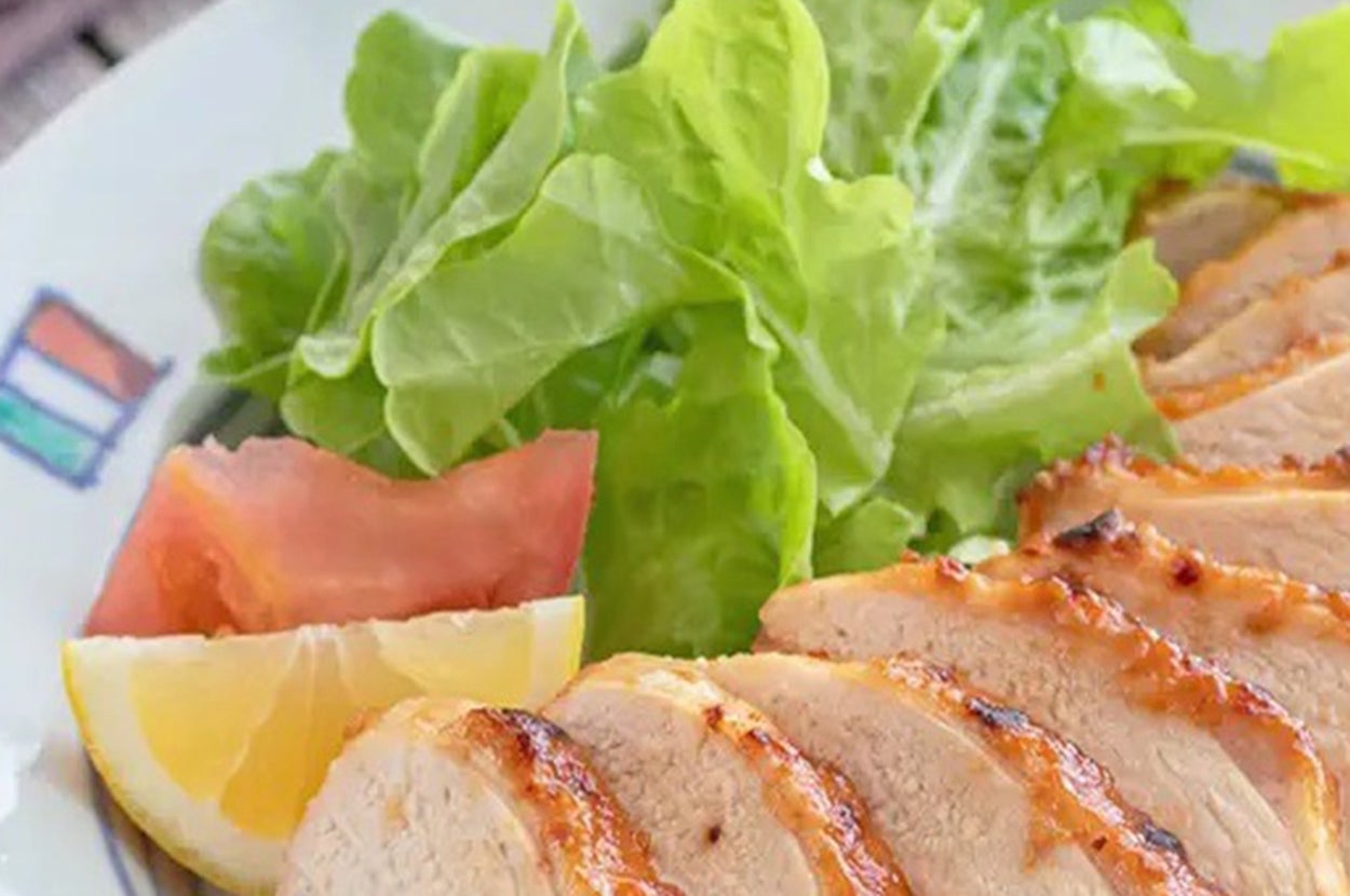 皿に盛られた焼き鶏のスライス、レタス、トマト、レモンが添えられた料理。