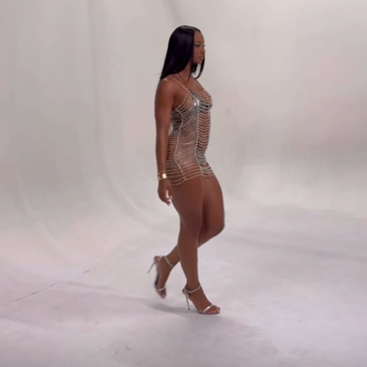 Kayla Nicole in a form-fitting, chain dress walking in a studio setting, wearing high heels