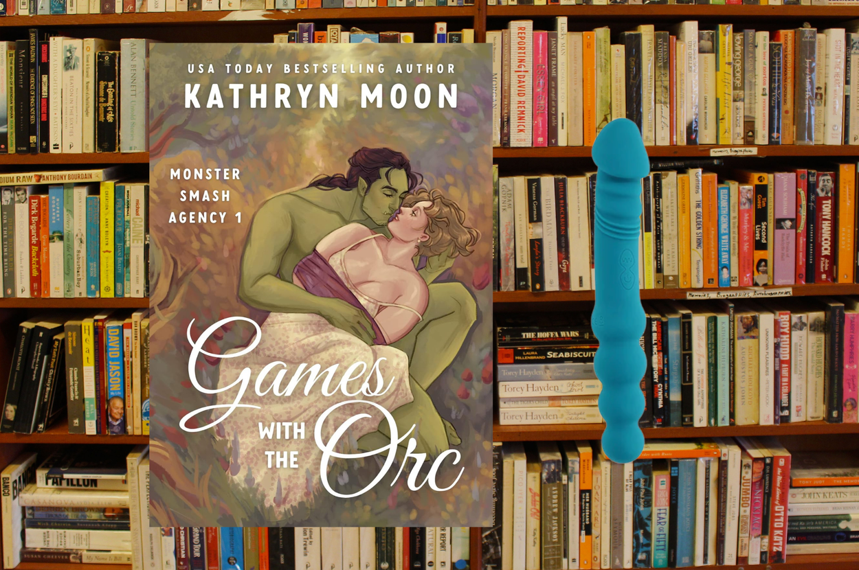 Book cover with an orc and woman embracing. Title: "Games with the Orc" by Kathryn Moon. Background: library shelves full of books