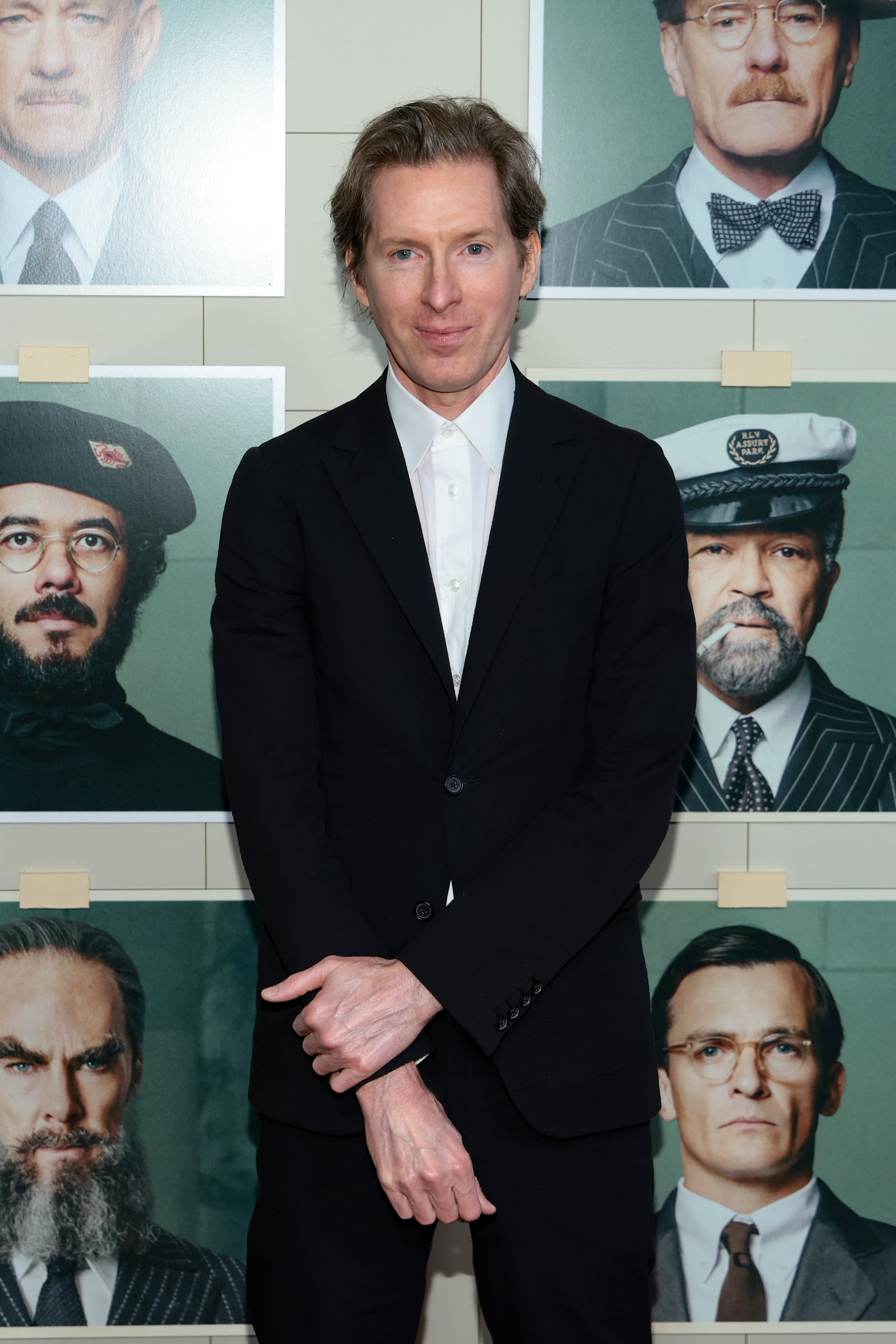 A idiosyncratic   successful  a sleek achromatic  suit   poses successful  beforehand   of a partition  displaying photos of individuals successful  assorted  costumes