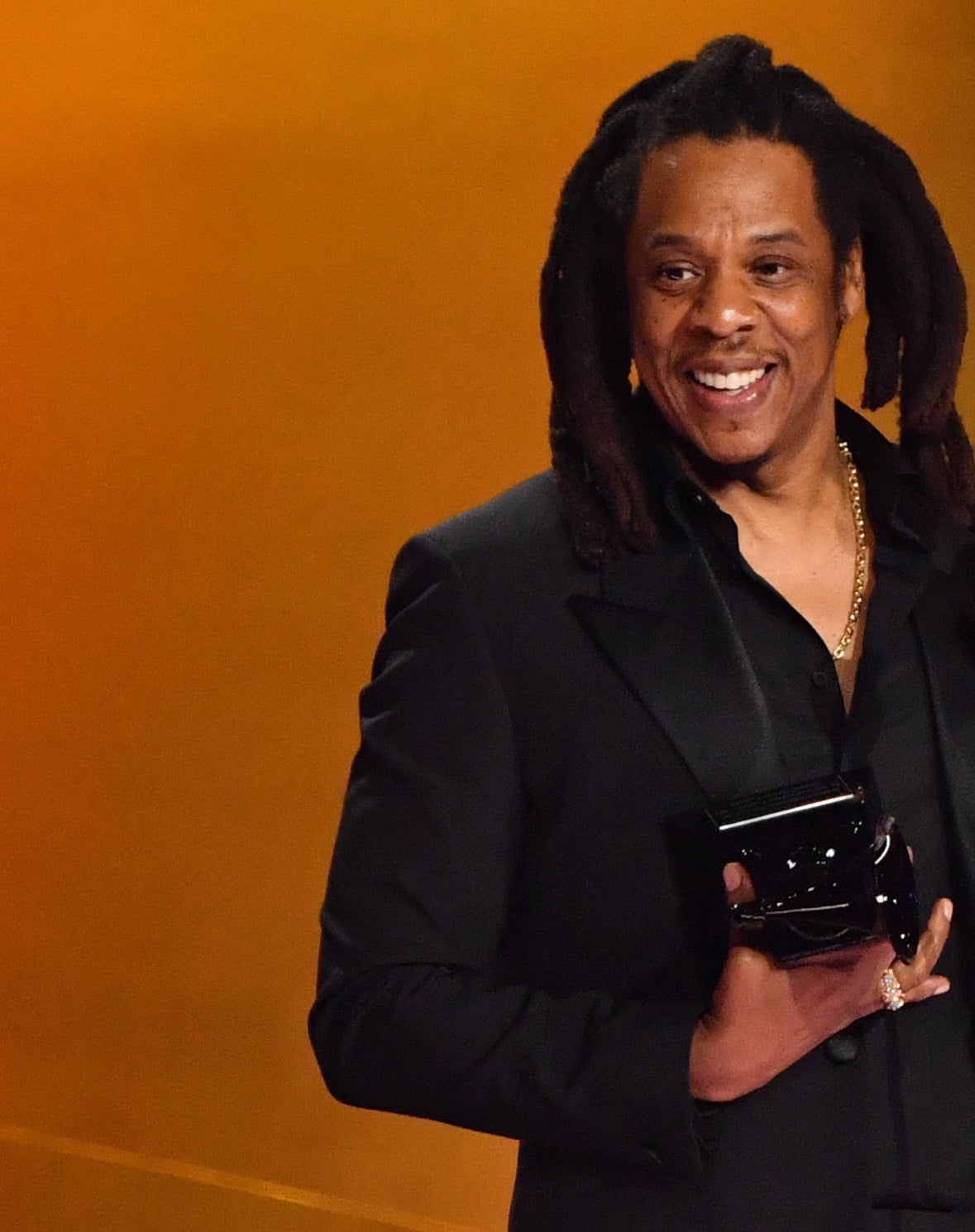 A antheral   with agelong  hairsbreadth  smiles portion    holding an grant  connected  stage, wearing a ceremonial  achromatic  suit   and shirt