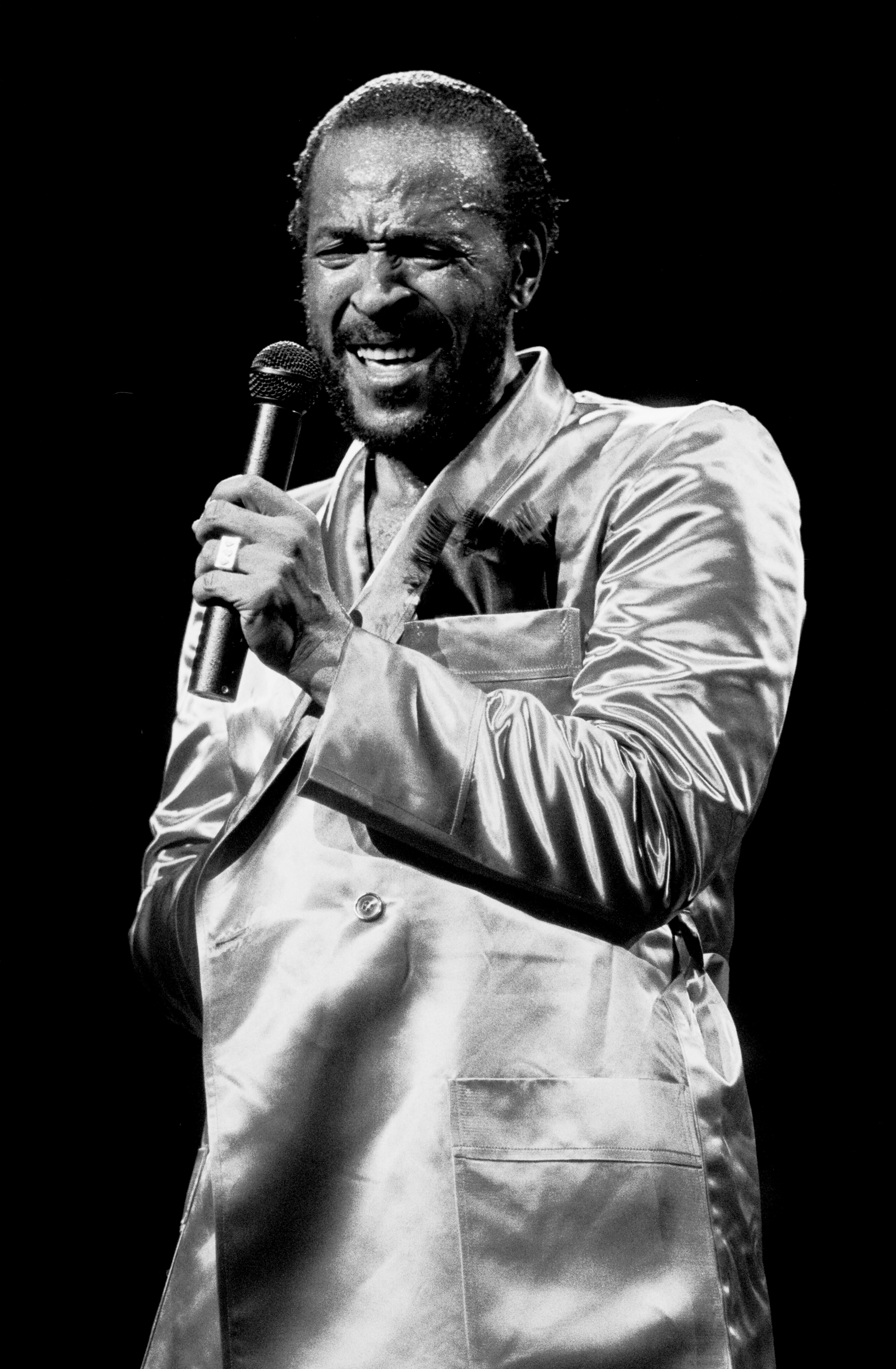 Person wearing a shiny suit   holds a microphone, performing with expressive emotion