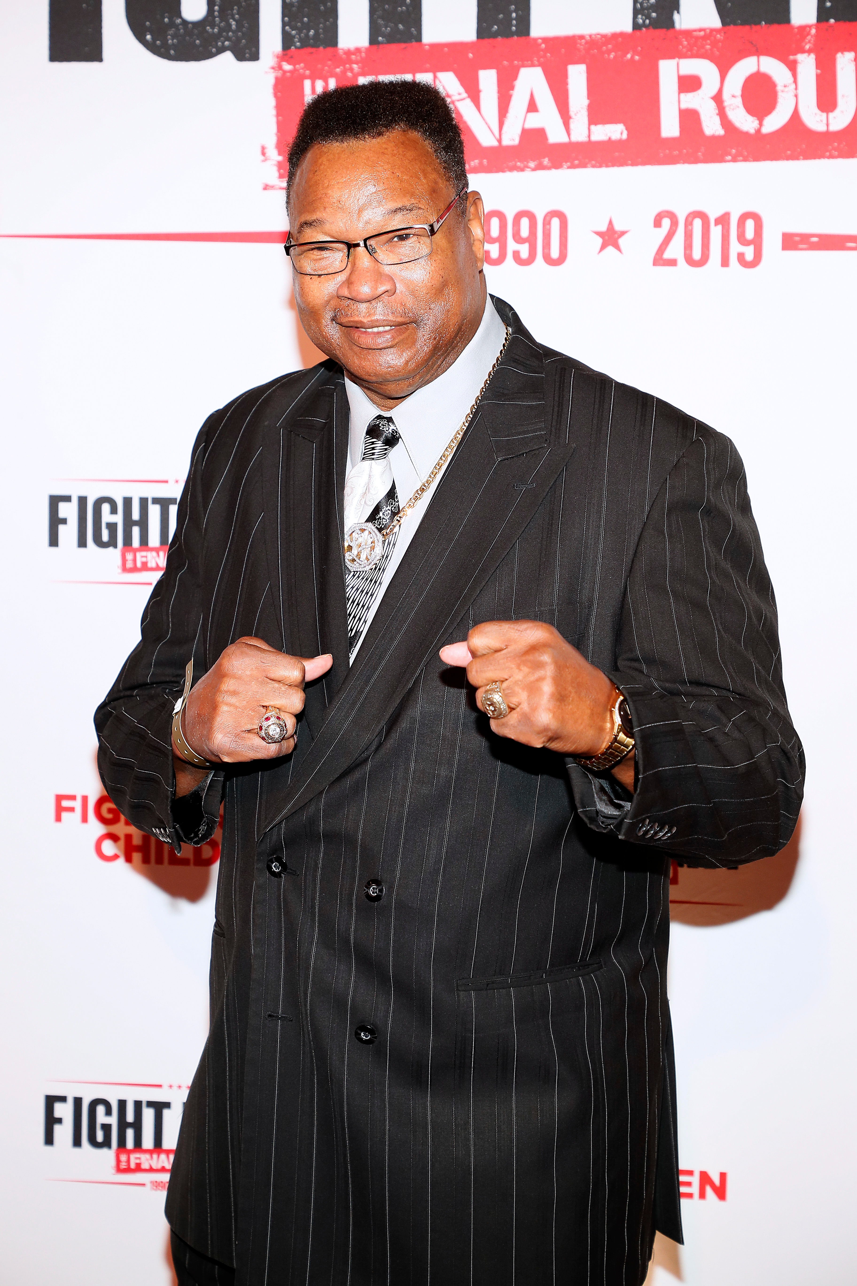 A idiosyncratic   poses confidently connected  the reddish  carpet, wearing a pinstriped suit   with a necktie  and bold jewelry, attending a personage  event