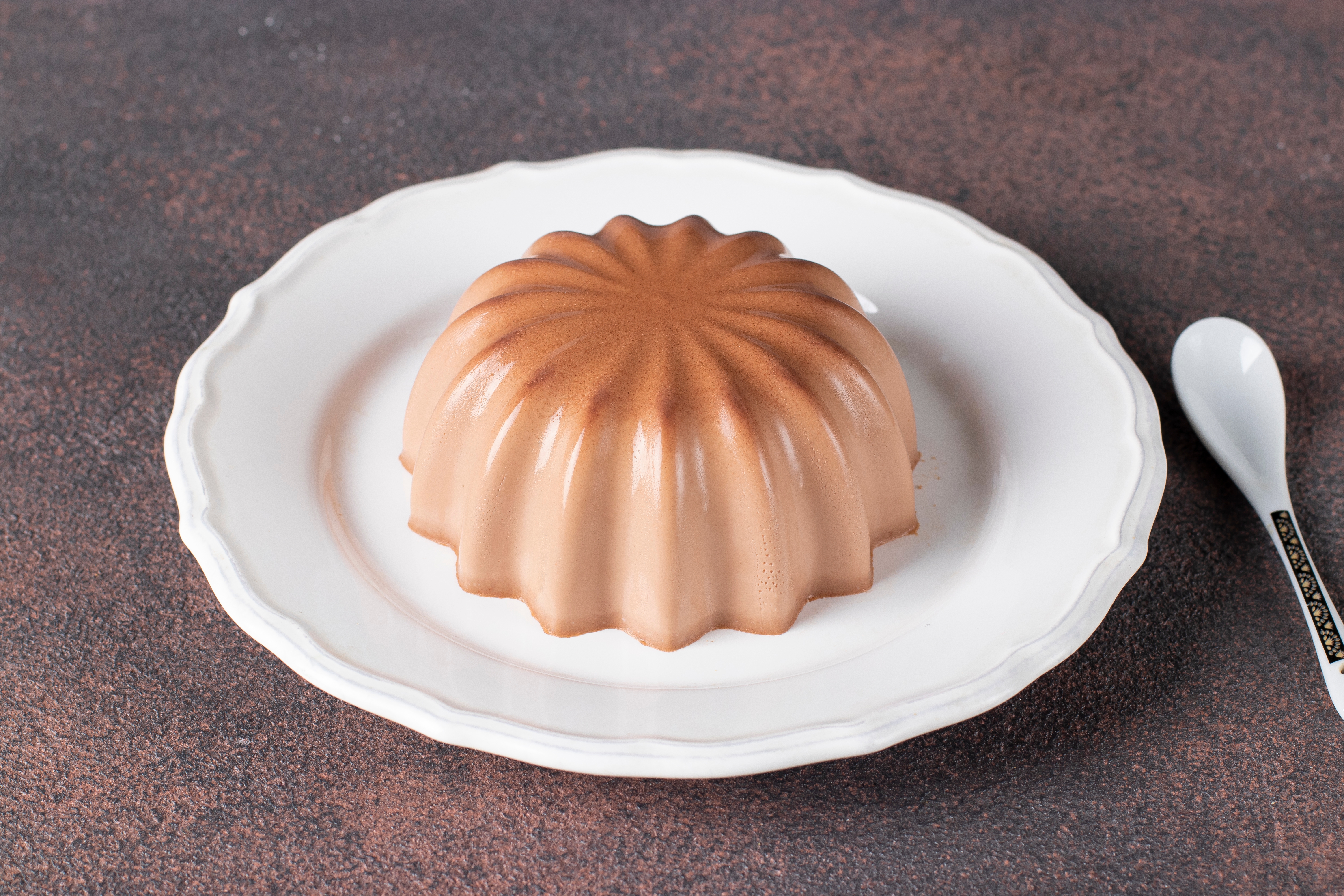 A chocolate mousse dome on a white plate with a spoon beside it