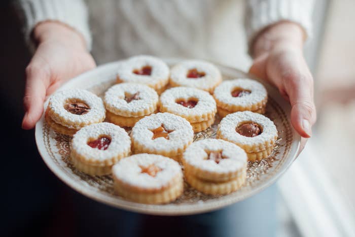 Person holding a plate of Linzer cookies, each with a different filling, dusted with powdered sugar