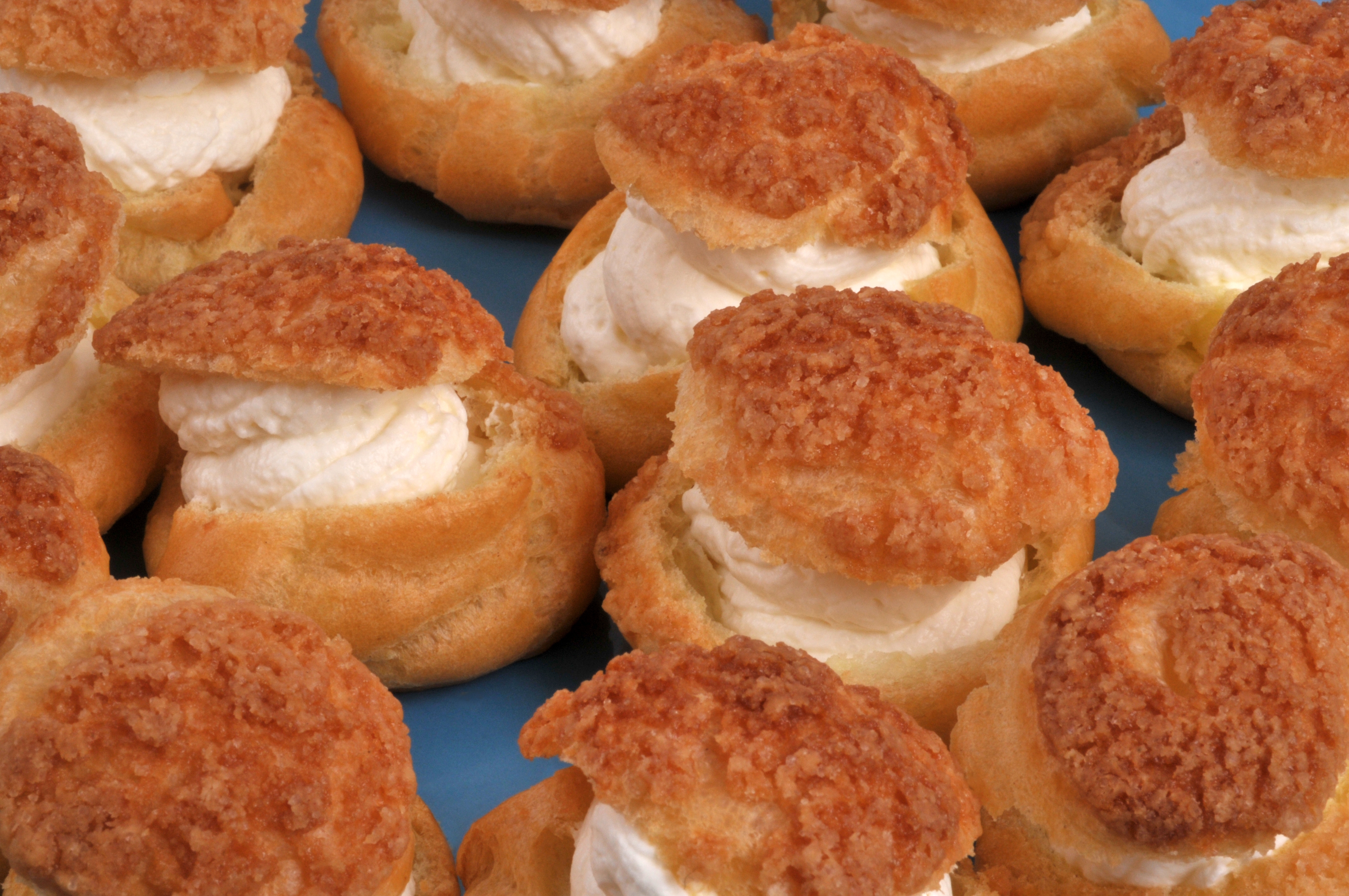 Cream puffs filled with whipped cream, topped with crispy, crumbly lids, arranged closely together on a platter