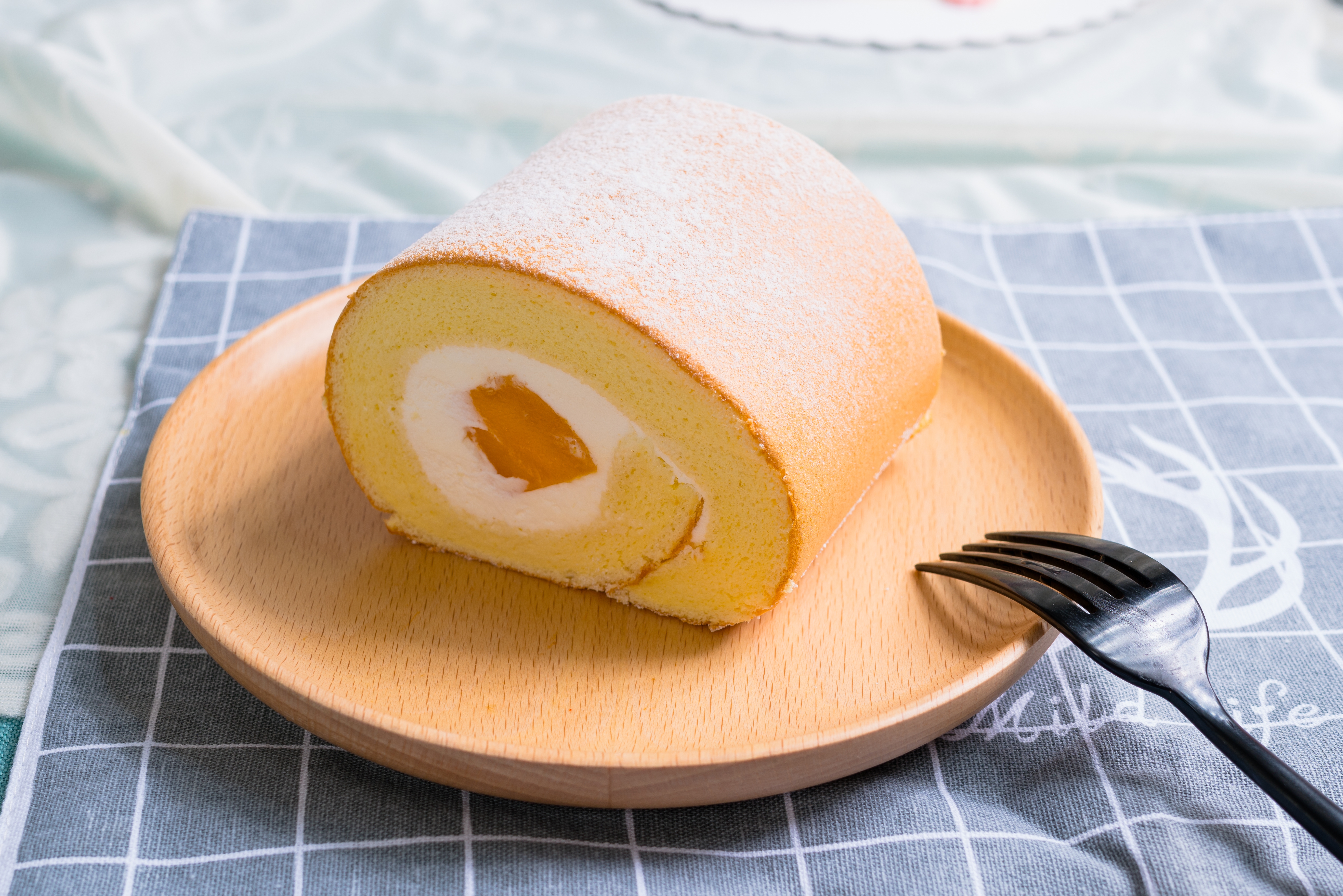 Swiss roll cake with a cream and fruit filling on a wooden plate, accompanied by a fork
