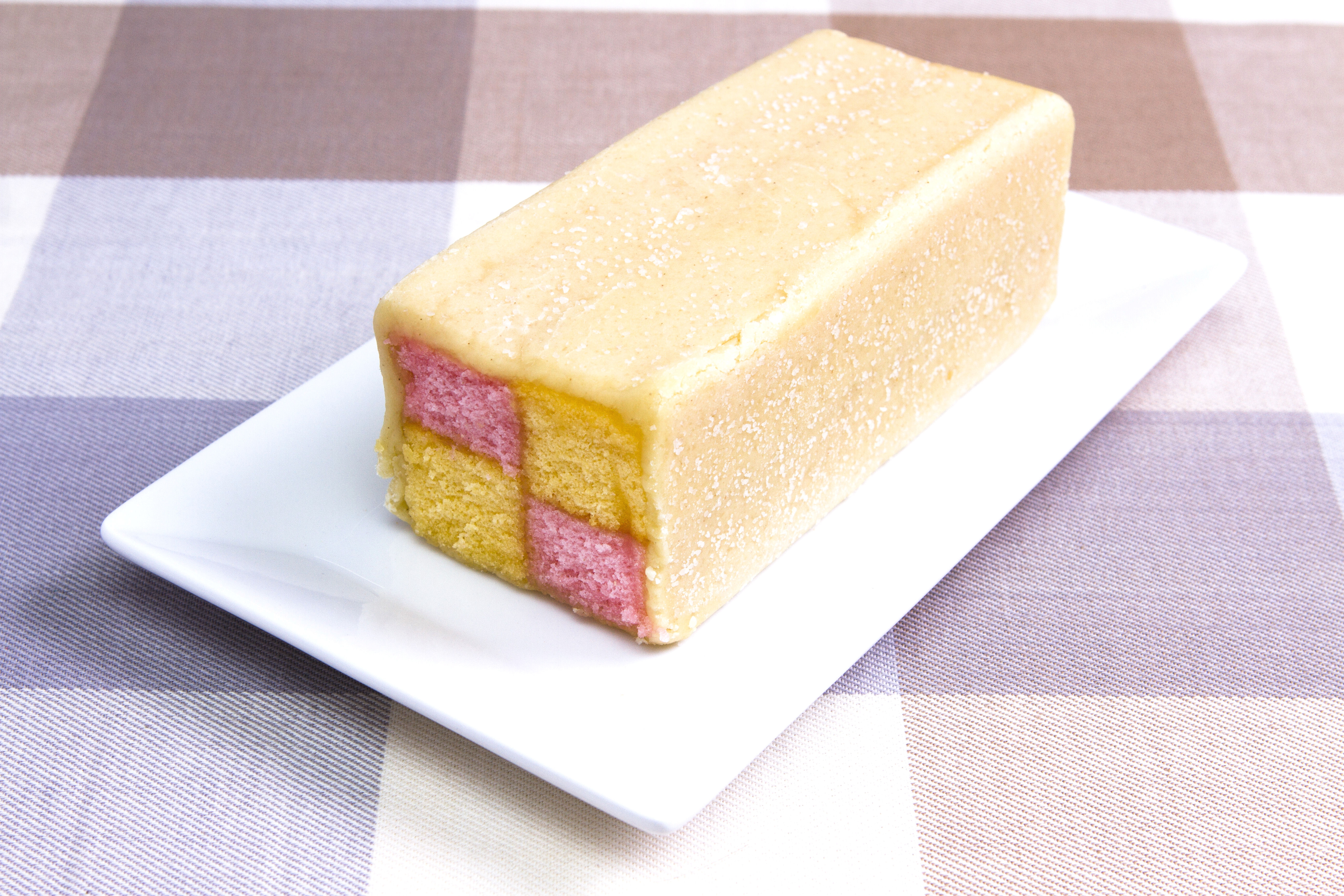 Battenberg cake on a white plate, featuring distinct yellow and pink sponge squares wrapped in marzipan