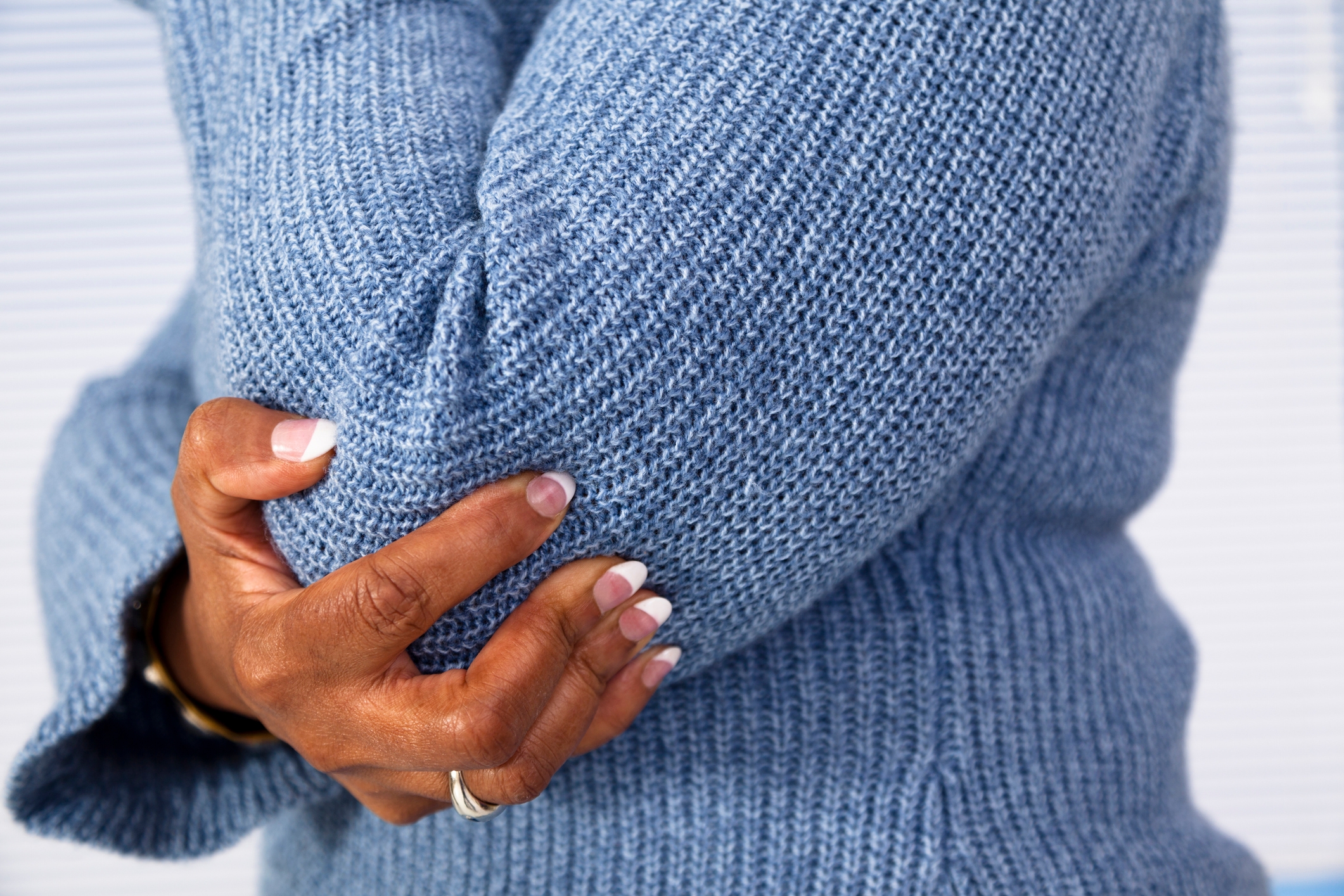 Person i en strikket genser som holder albuen med én hånd, negler velstelt med en fransk spiss