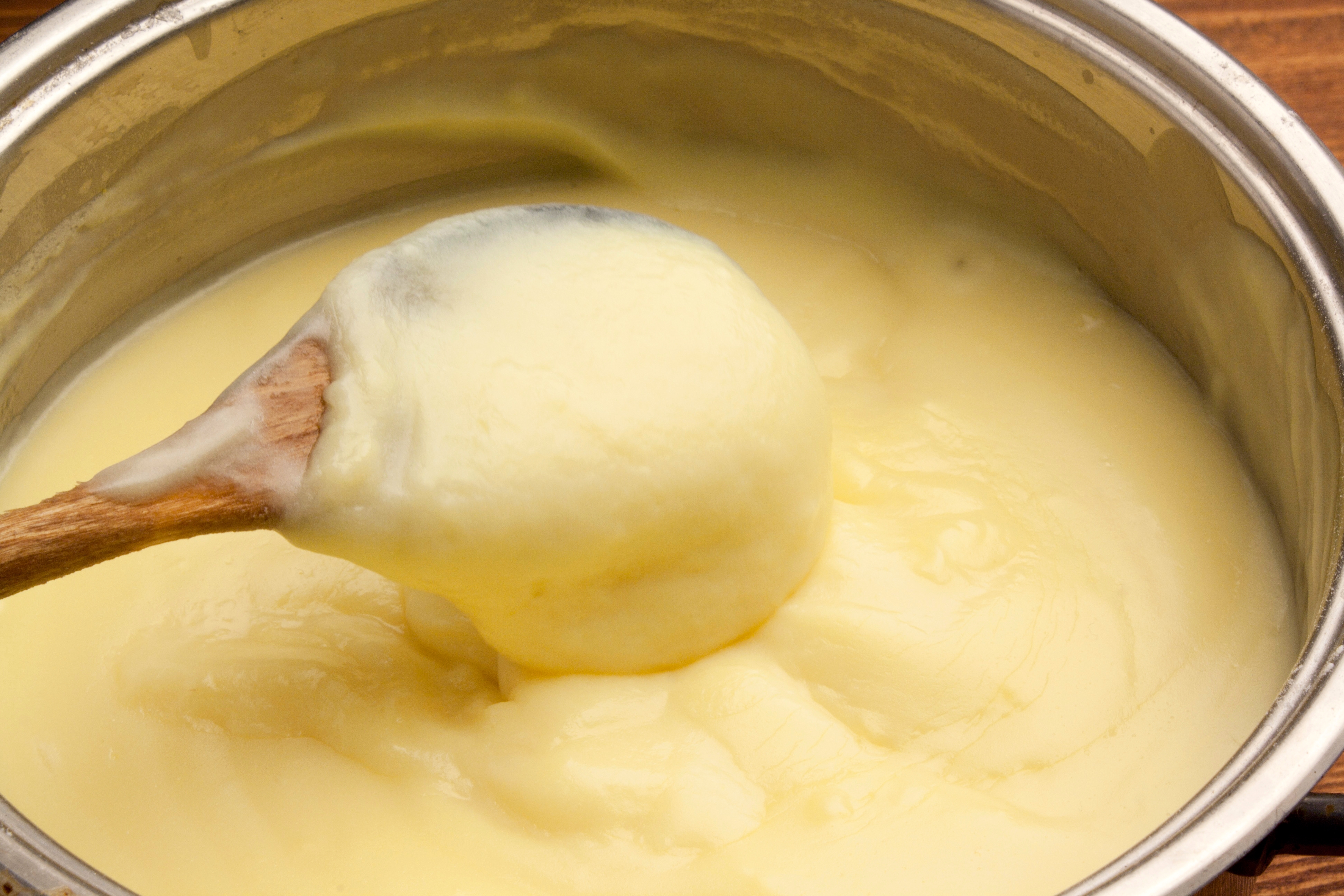 Thick, creamy custard being stirred in a saucepan with a wooden spoon