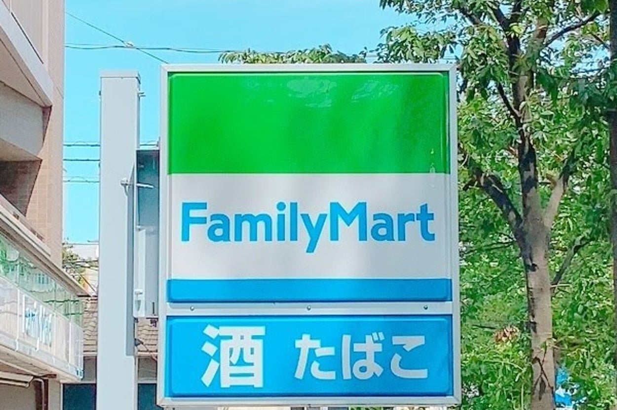 通りにあるファミリーマートの看板。「酒」「たばこ」の文字が見える。周囲には建物と木々がある。