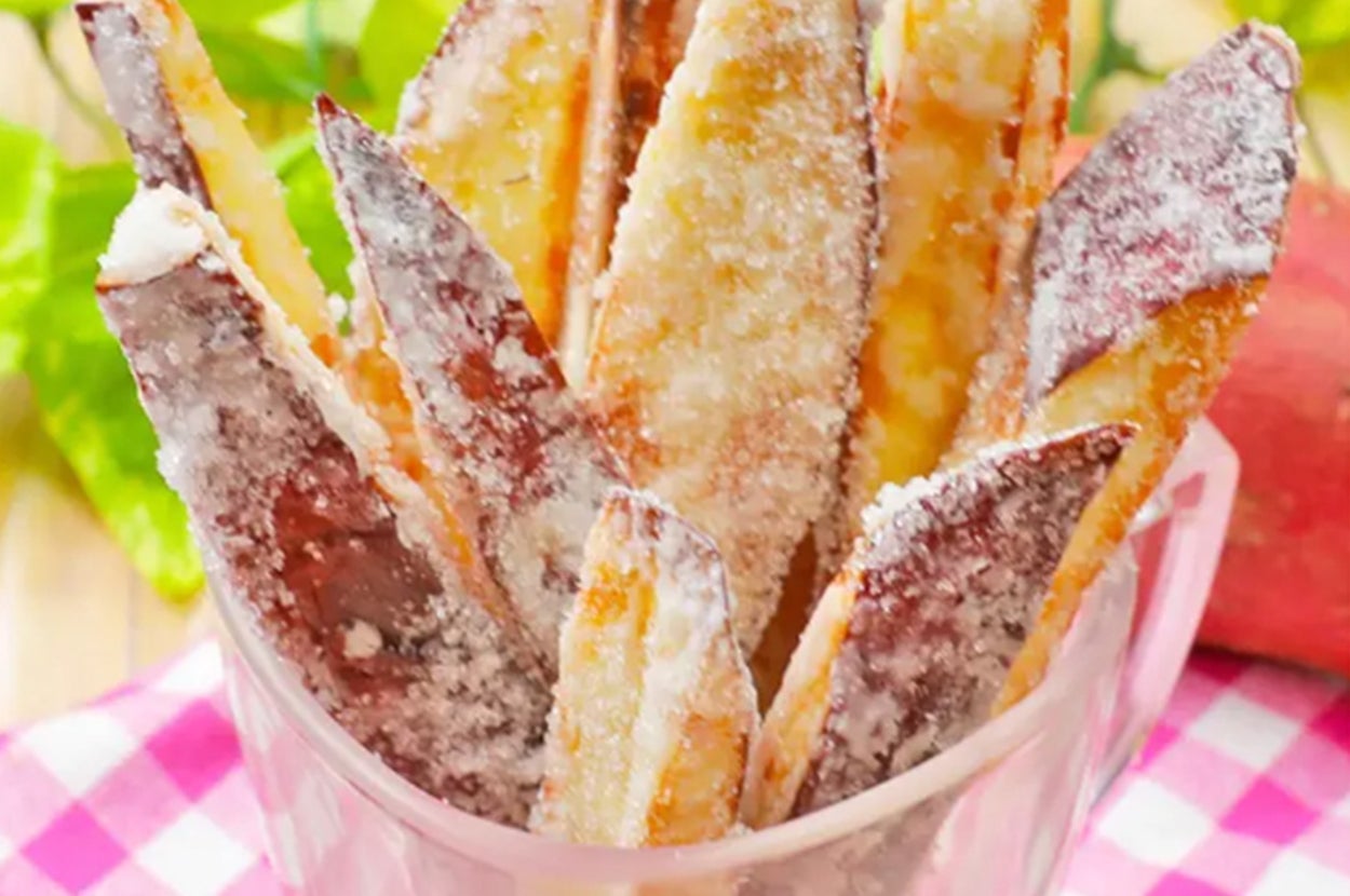 砂糖がまぶされたスティック状の揚げたサツマイモがカップに入っている。背景に葉とチェック柄の布が見える。