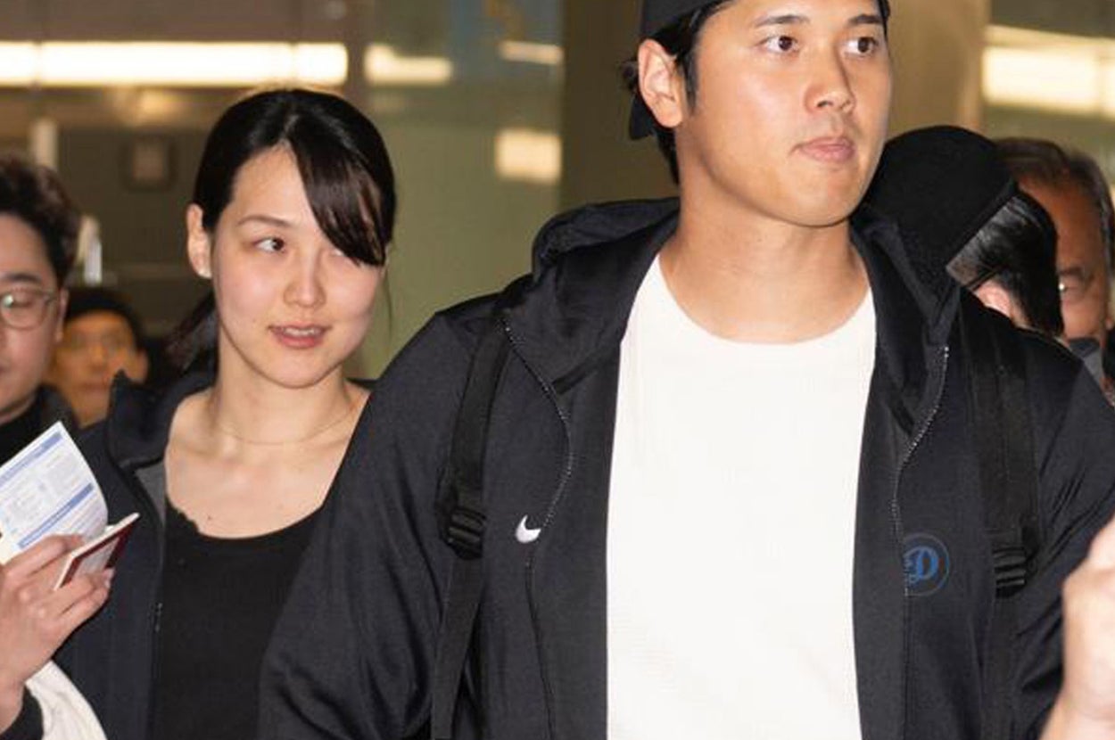 男性がカジュアルな服装で空港に到着し、ファンがその様子を写真に収めている。