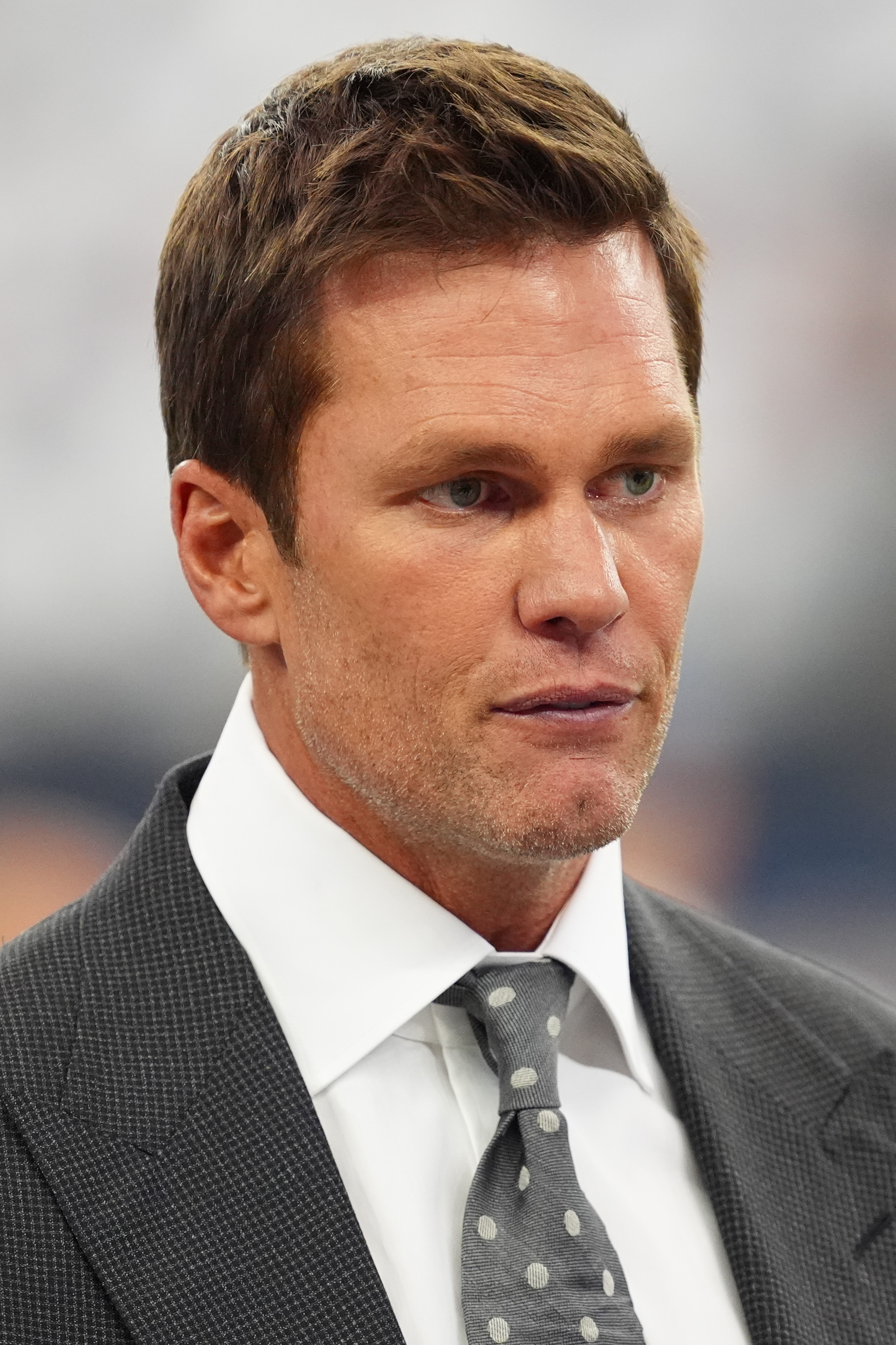 Tom Brady in a suit and polka dot tie attending an event, looking thoughtful