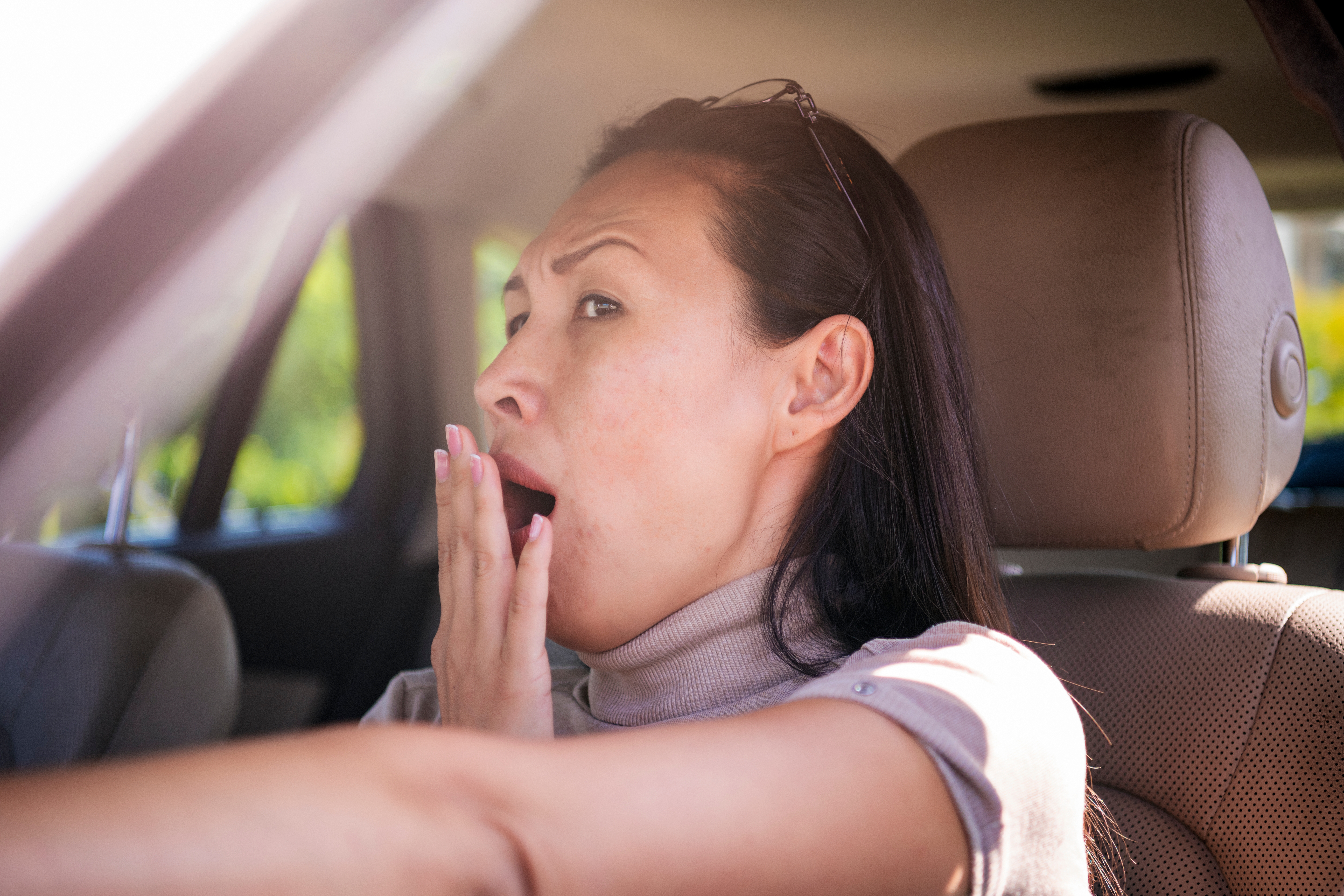 Person som gjesper mens han sitter i en bil, hånden dekker munnen, virker trøtt