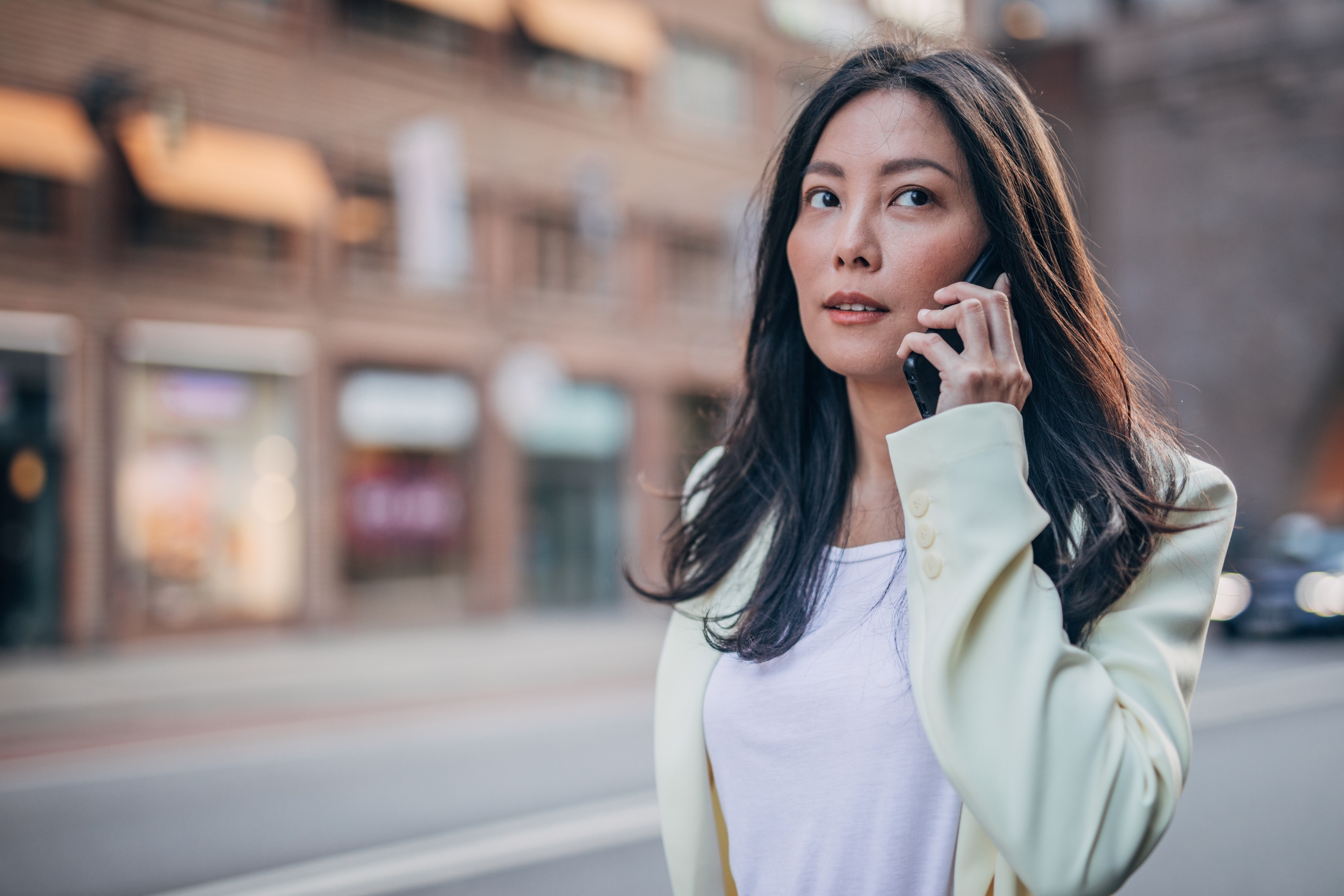 En kvinne i en hvit blazer snakker i telefonen hennes og går i en bygate