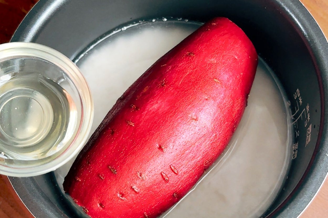 炊飯器の内釜に洗ったサツマイモと水が入っている。部屋の木製のテーブルの上に置かれている。