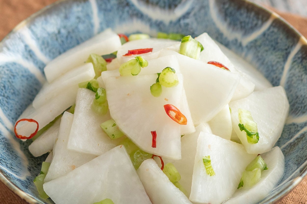 薄切りの大根とねぎ、唐辛子が調和されたサラダが陶器の器に盛られている。