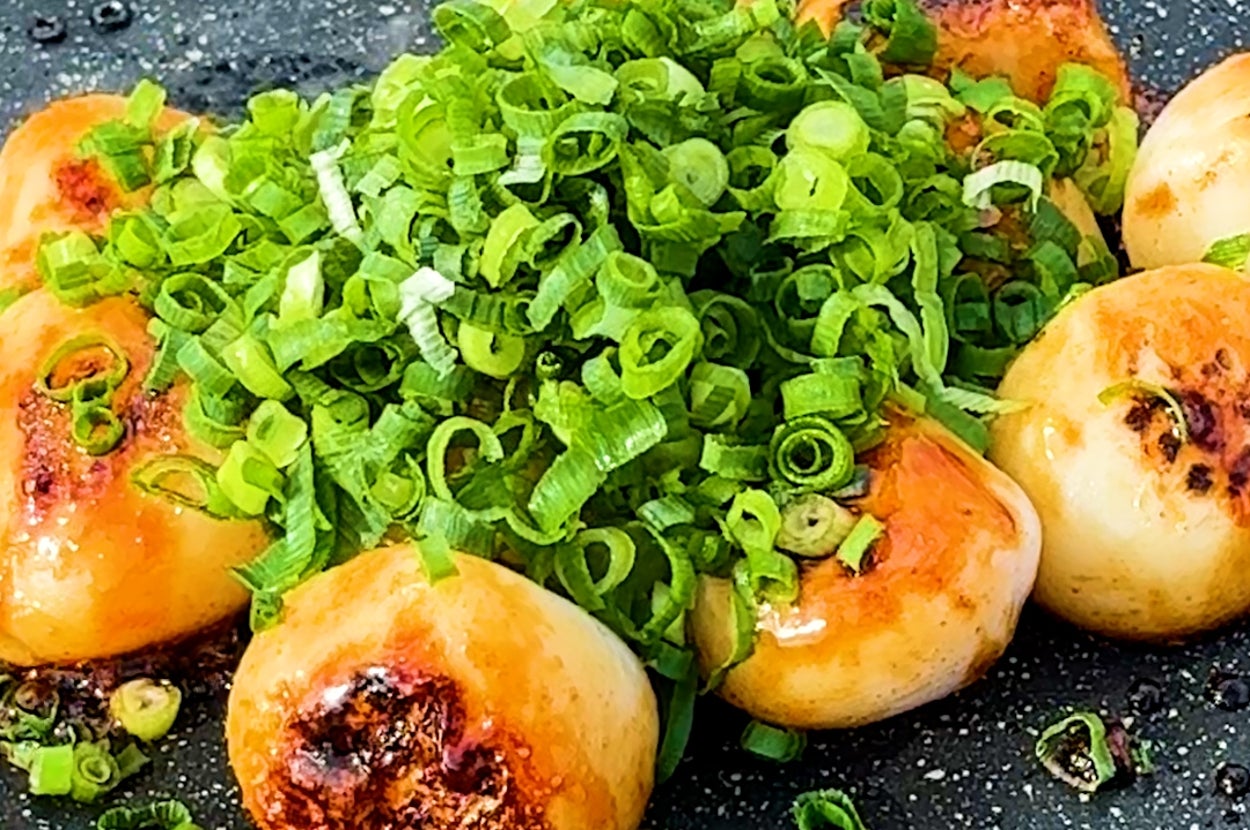 ネギがたっぷり乗った焼き餃子が黒いプレートに盛られている。