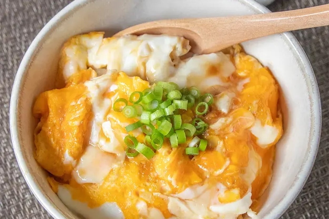 卵とネギがトッピングされたどんぶり料理が、テーブル上の木製スプーンと共に置かれている。