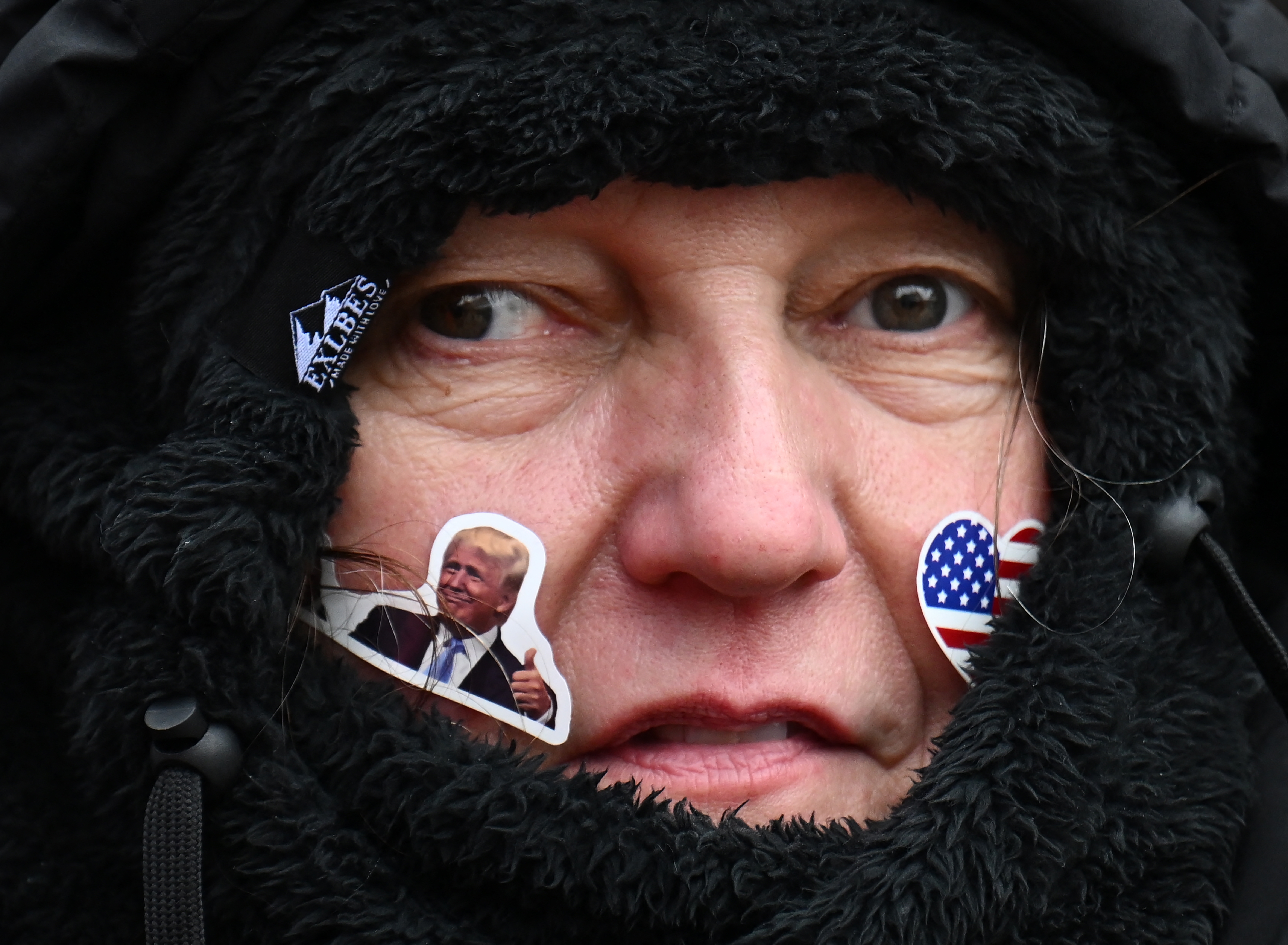 Person samlet i svart frakk med klistremerker i ansiktet: en av en person som viser tommel opp, og en annen med hjerteformet amerikansk flaggdesign